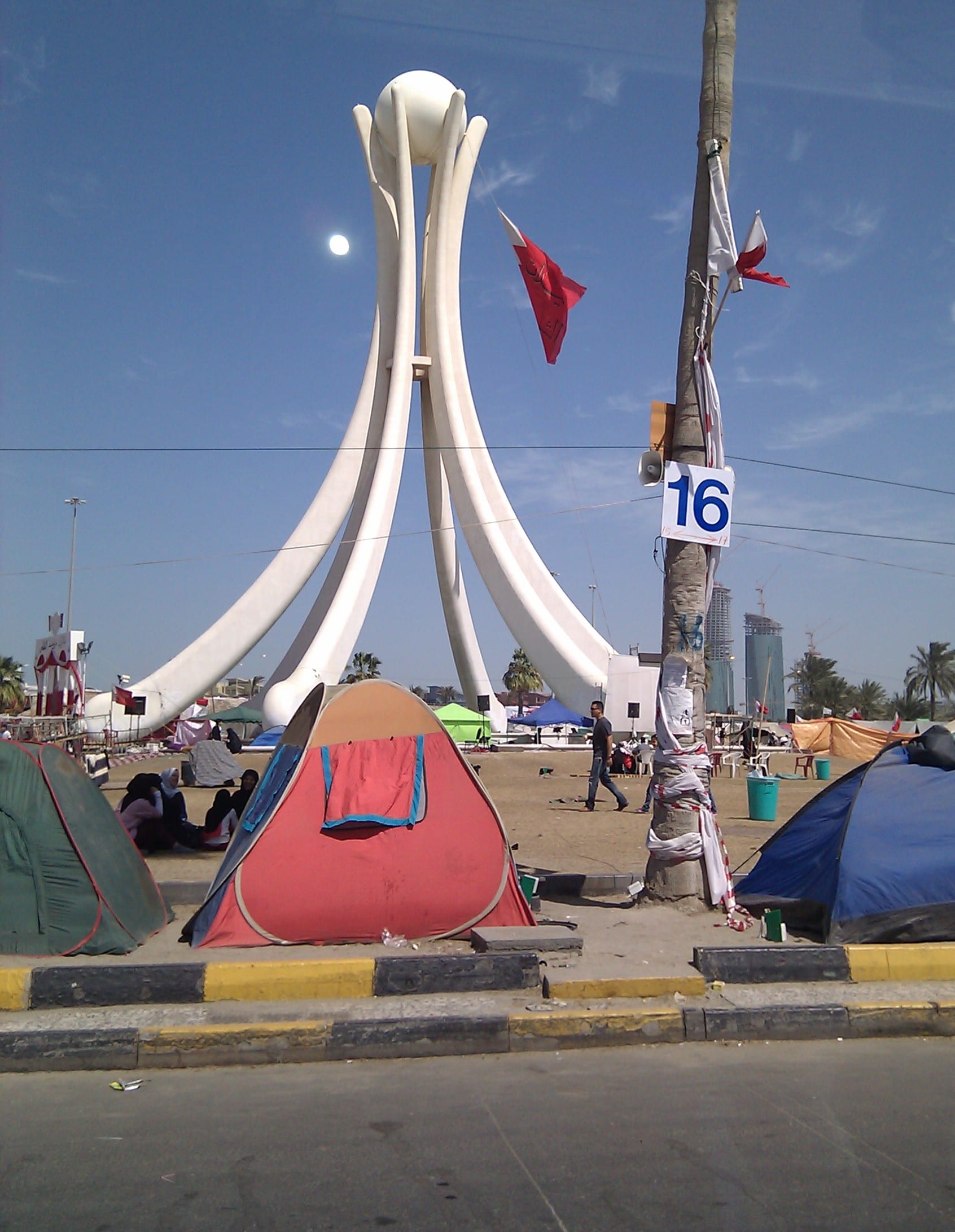 A large night-time crowd of protesters with tents and Bahraini flags gathered around a tall monument