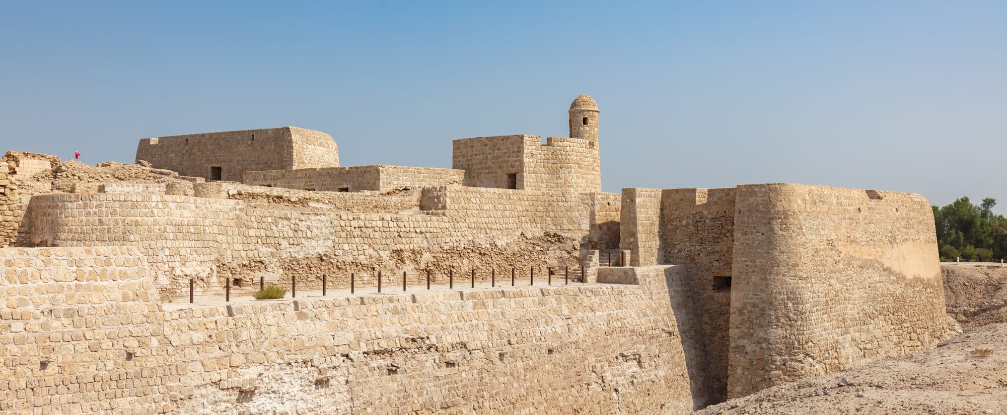A pale stone fort with corner bastions rising from a grassy archaeological mound beside the sea