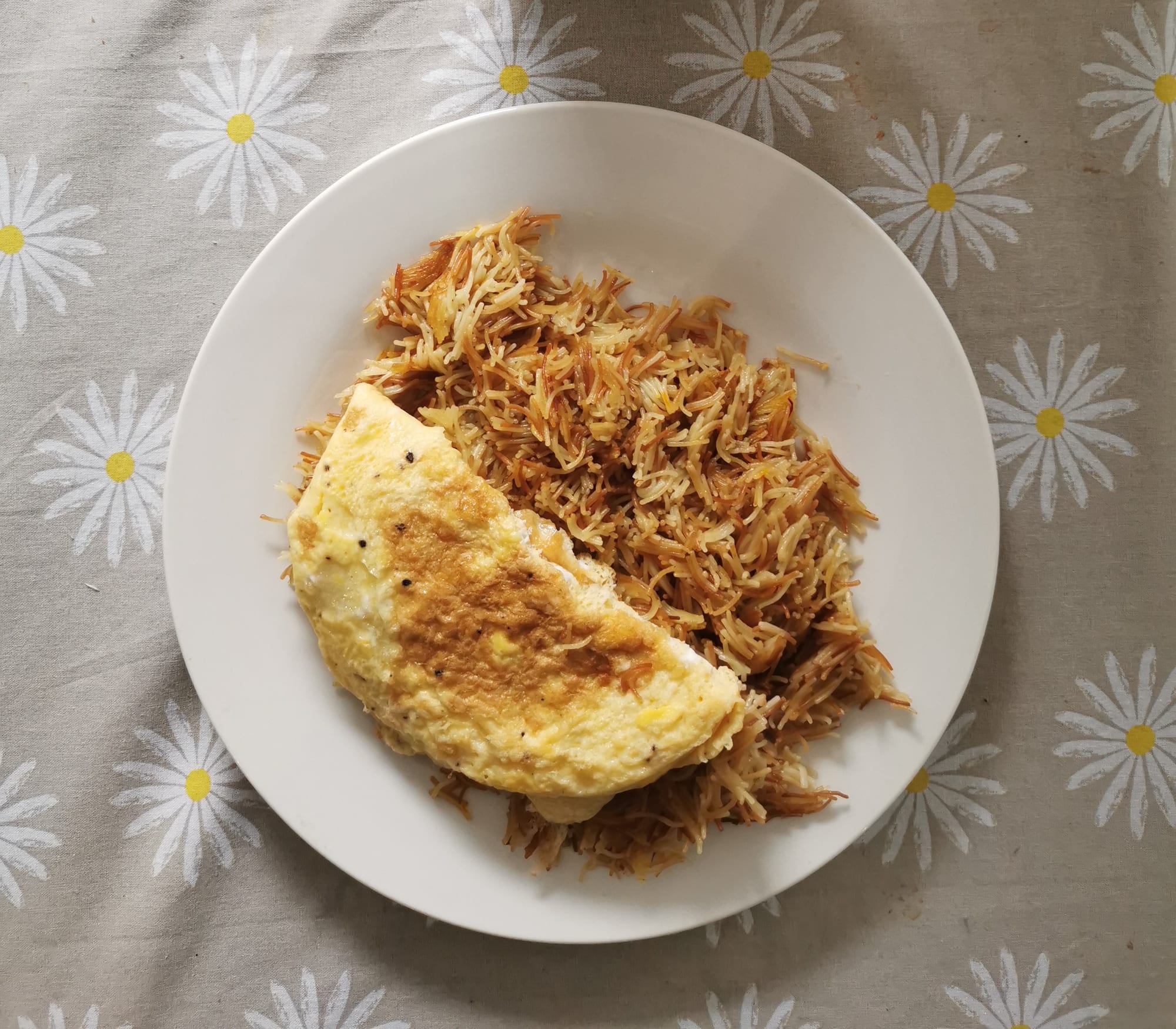 A plate of orange-tinted sweet vermicelli noodles topped with a folded savoury omelette