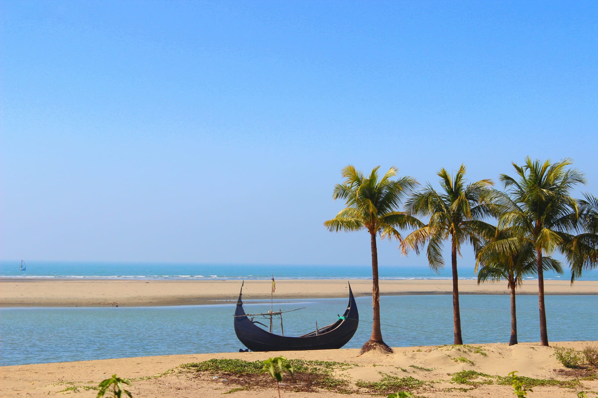 A sandy beach with palm trees and a traditional wooden boat, calm sea beyond