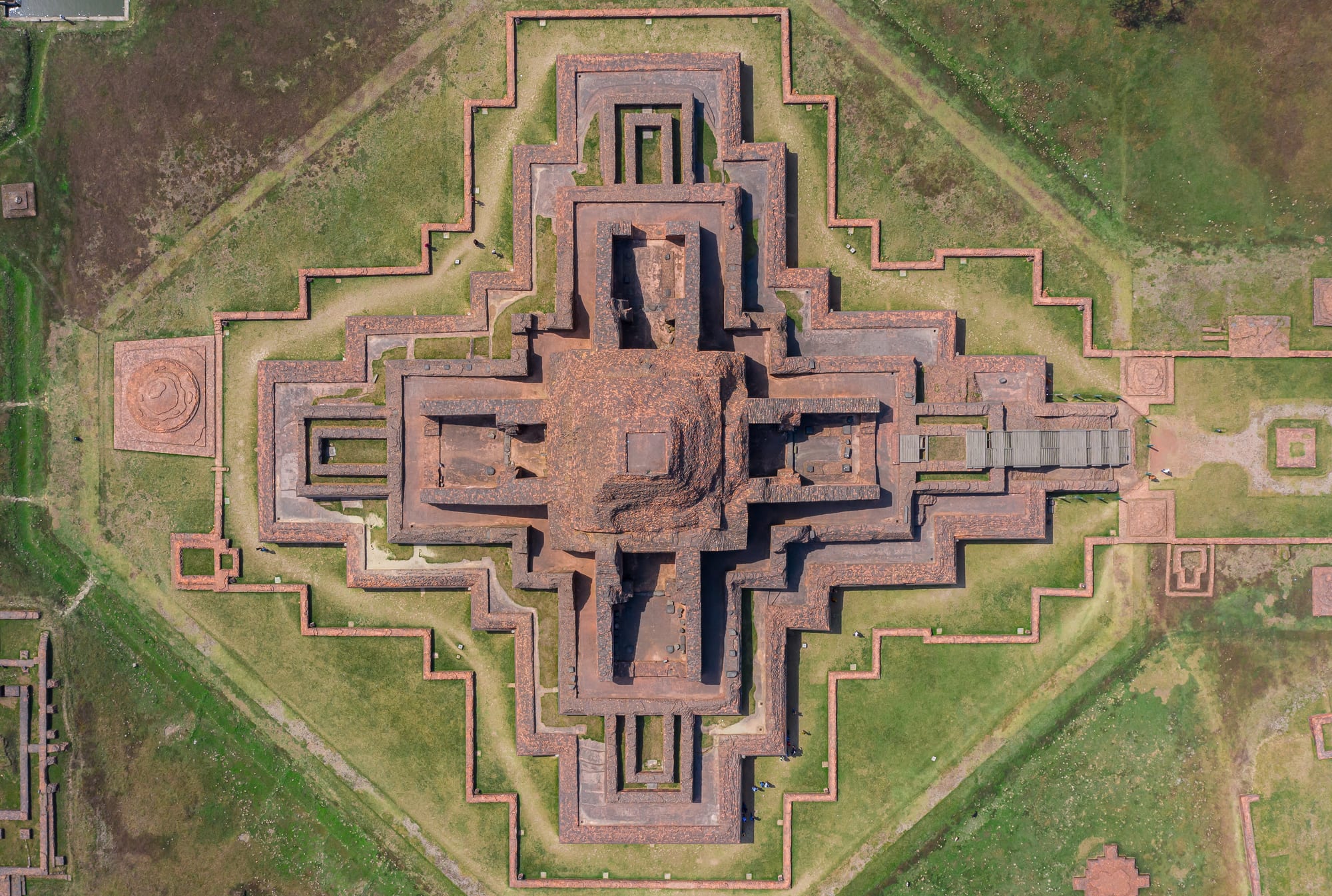A huge square monastery ruin with a stepped central shrine, seen from above
