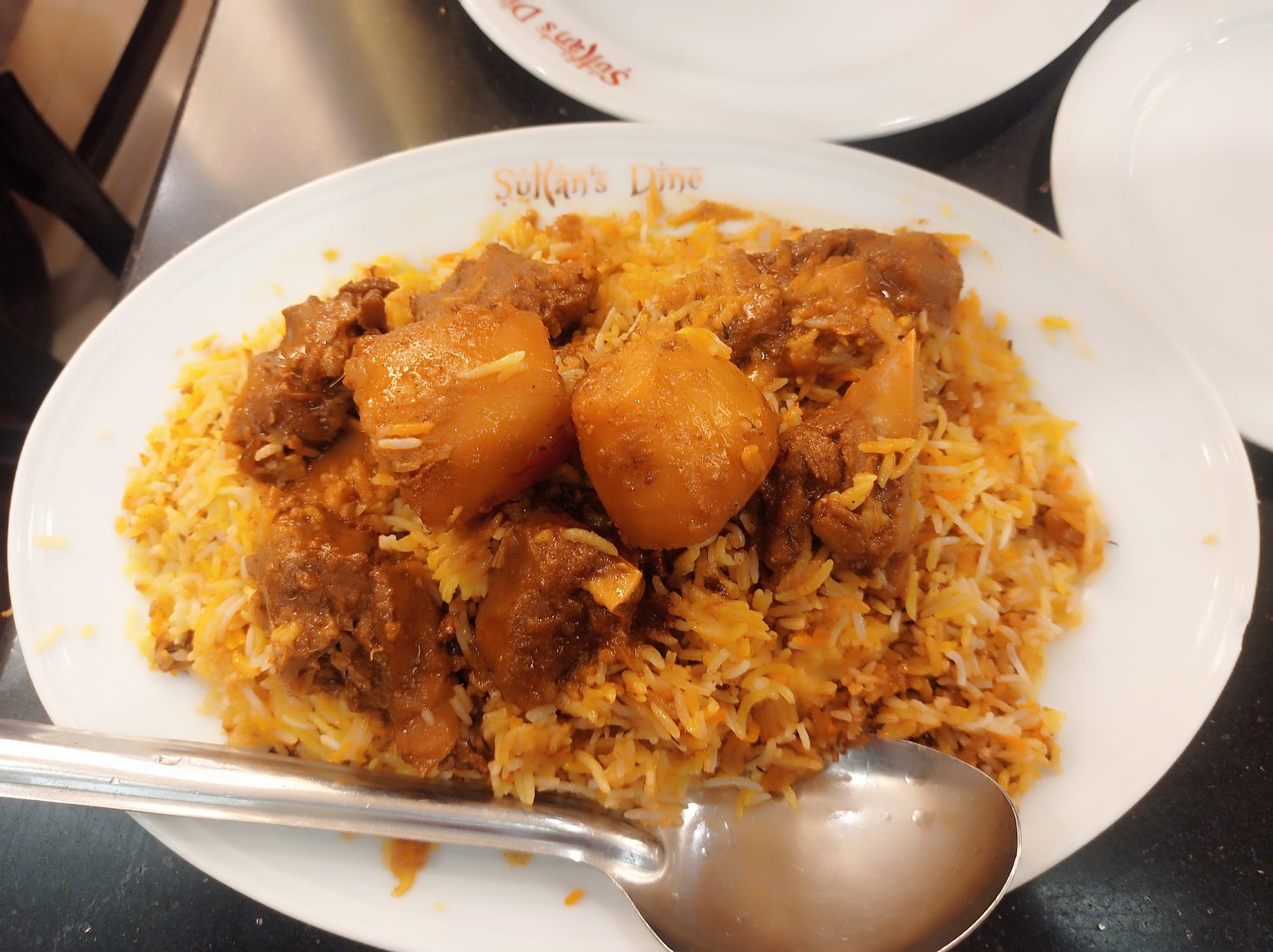 A large plate of golden, spiced rice with a piece of meat on top, garnished with fried onions