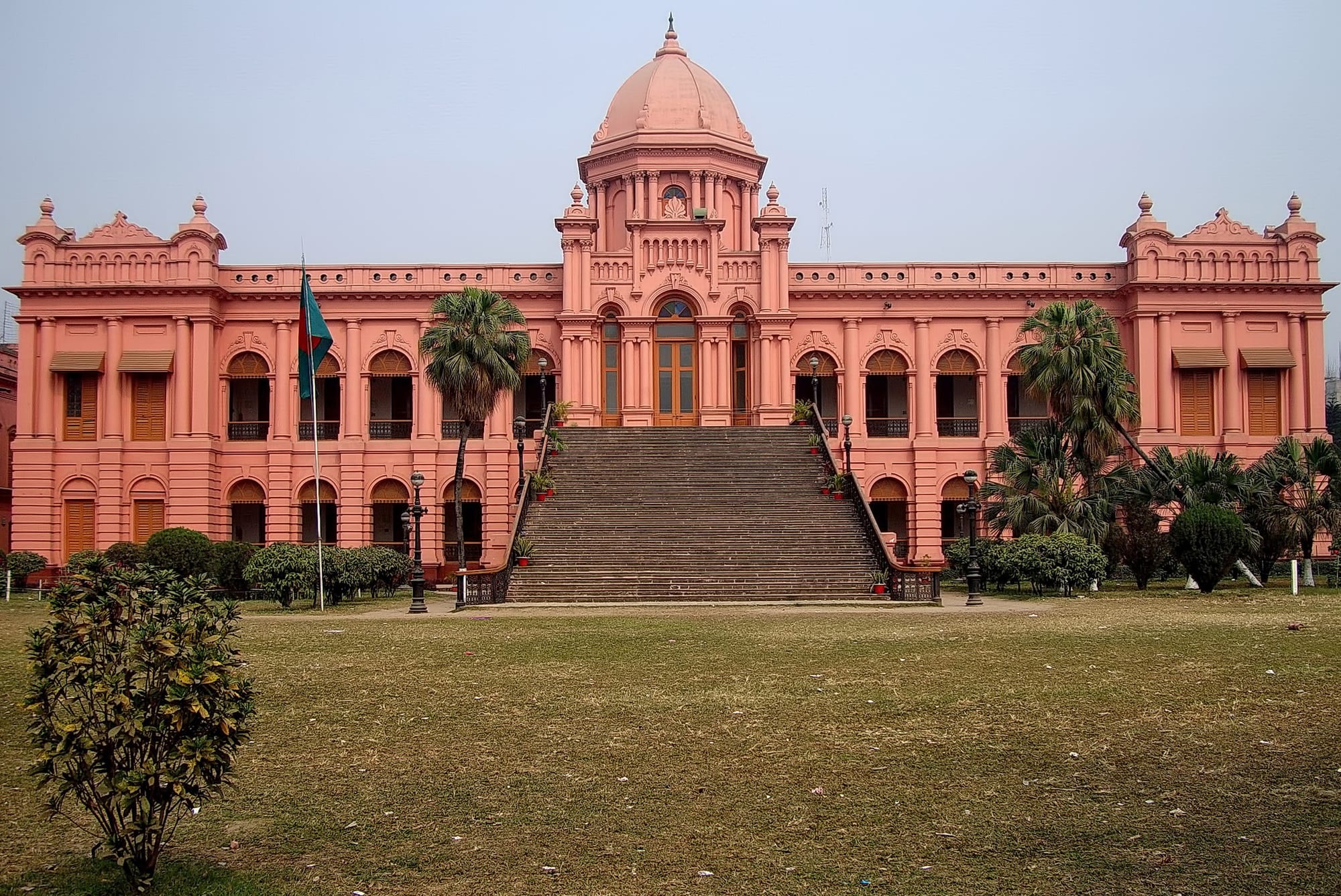 A large pink two-storey palace with a central dome and wide steps down to a river