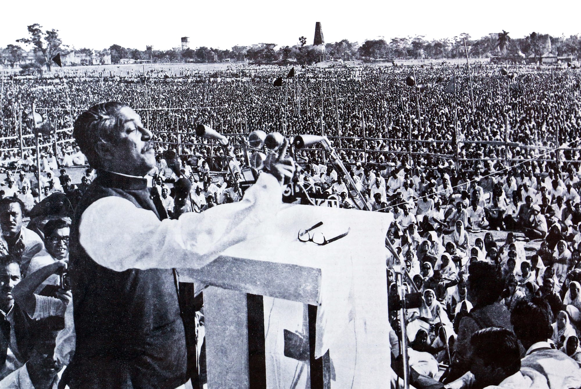 A man at a microphone-covered rostrum addressing an enormous crowd filling a field