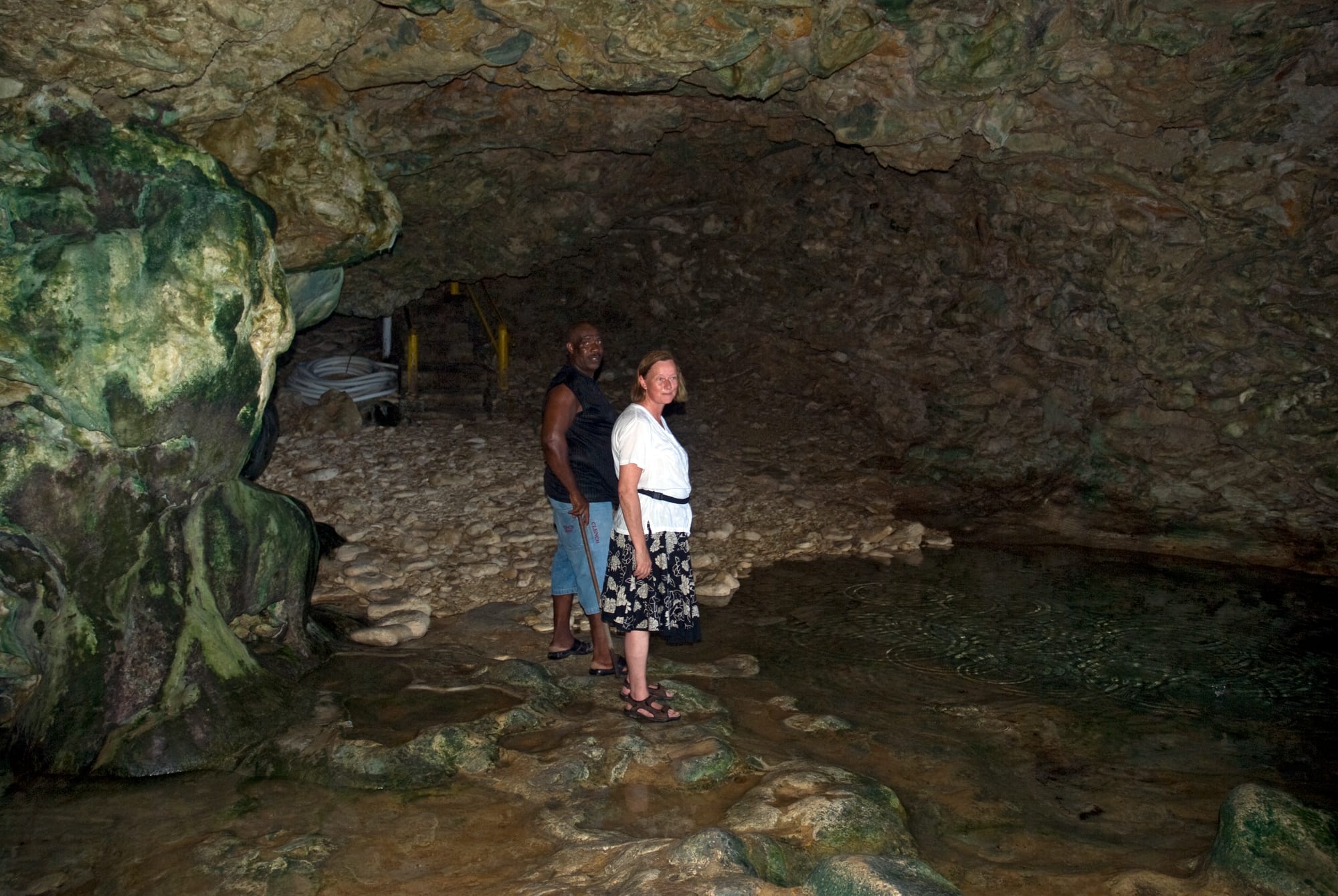 A sea cave opening onto the ocean, waves visible through the mouth, rock pools inside