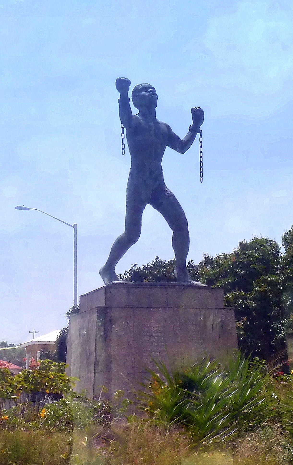 A bronze statue of a muscular man with arms raised and broken chains hanging from his wrists
