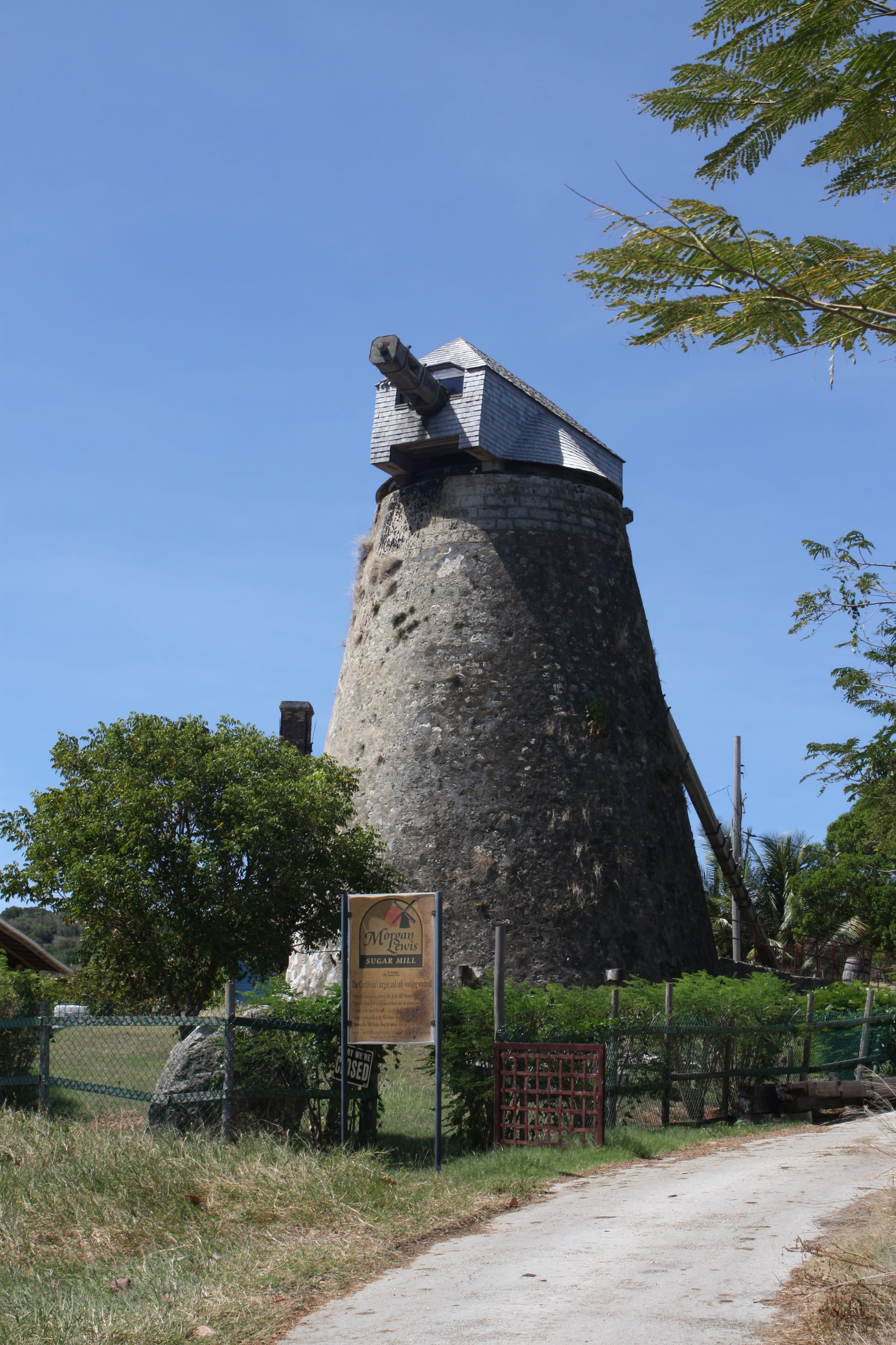 A tall stone tower windmill with wooden sails and a conical cap standing on a green hilltop