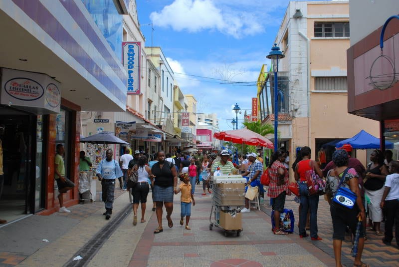 A crowded pedestrianised shopping street in Bridgetown with shoppers, vendors and umbrellas outside storefronts