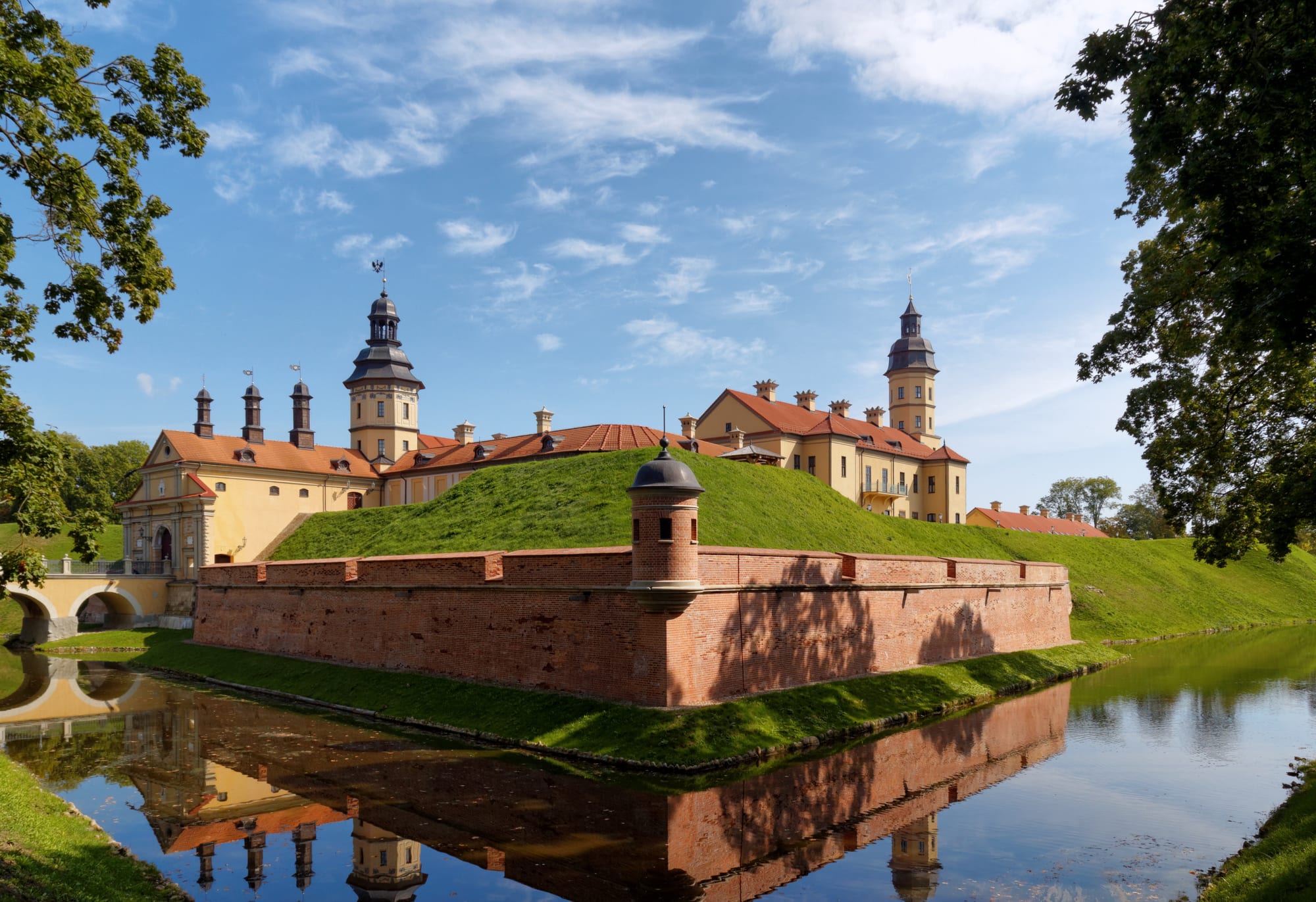 A long white palace with towers and a gatehouse behind a moat and bridge