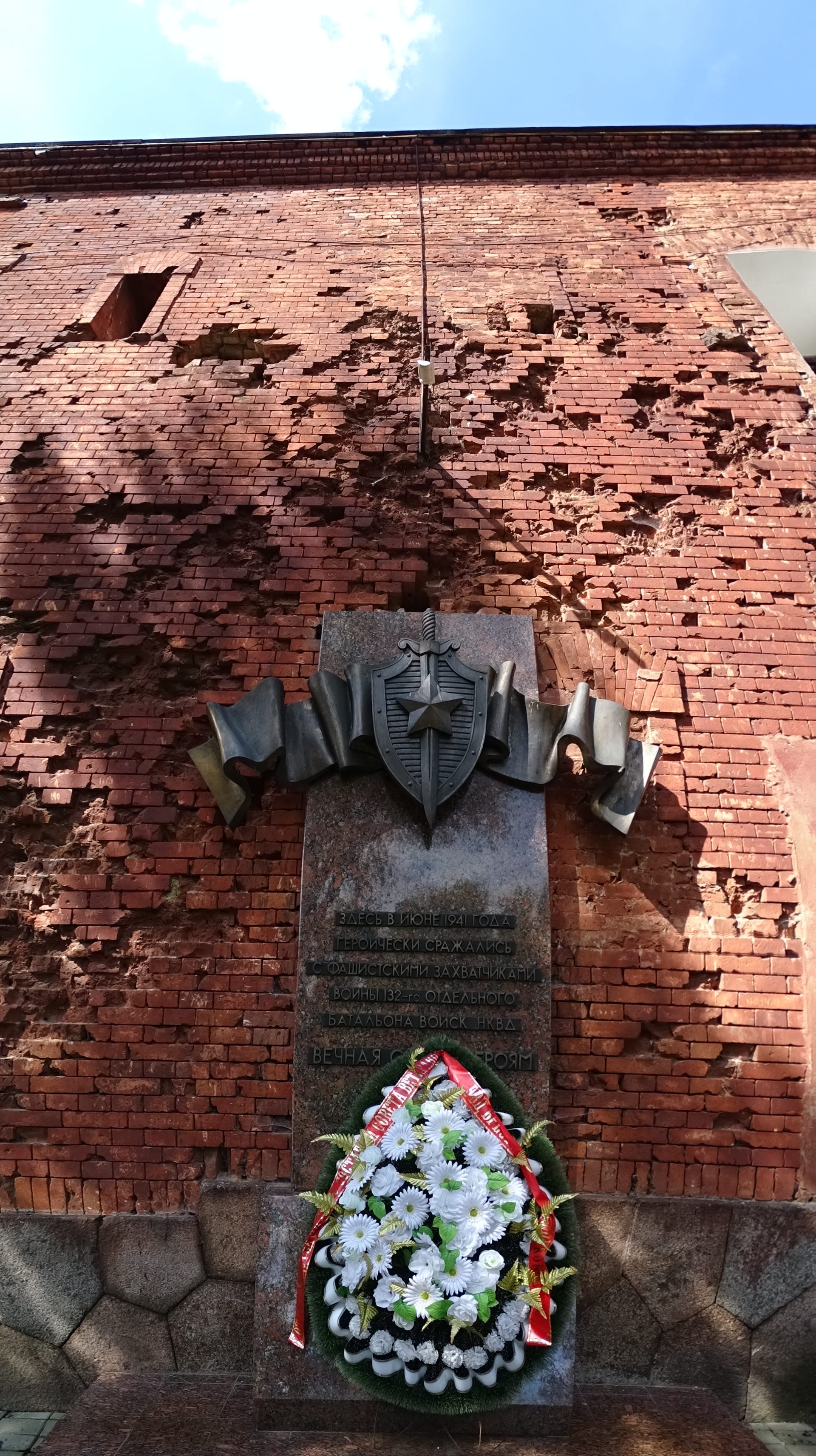 A colossal concrete head carved from a cliff of rock, beside a ruined brick barracks