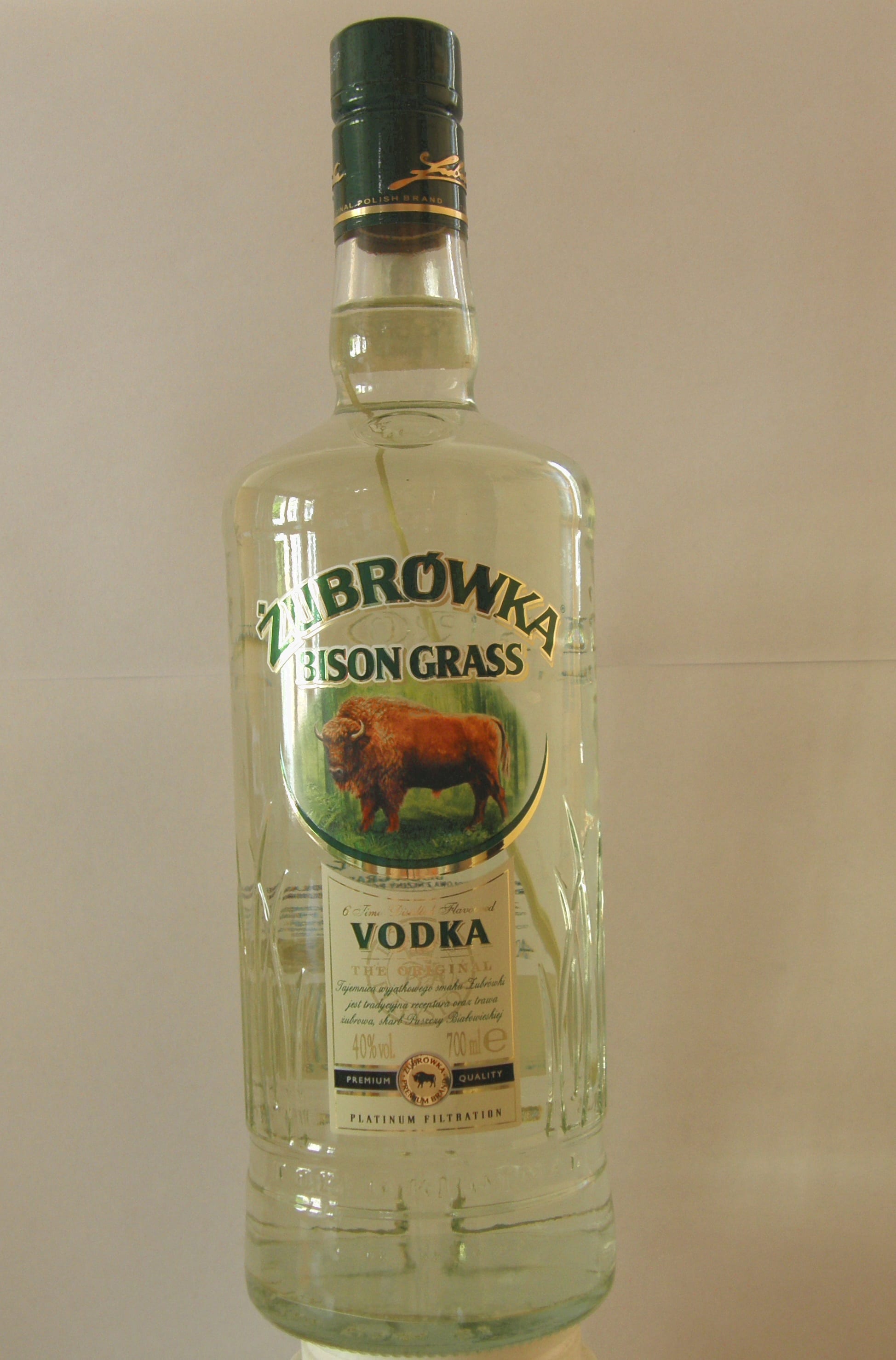 A tall bottle of pale yellow-green vodka labelled Żubrówka Bison Grass, with an image of a bison on the label