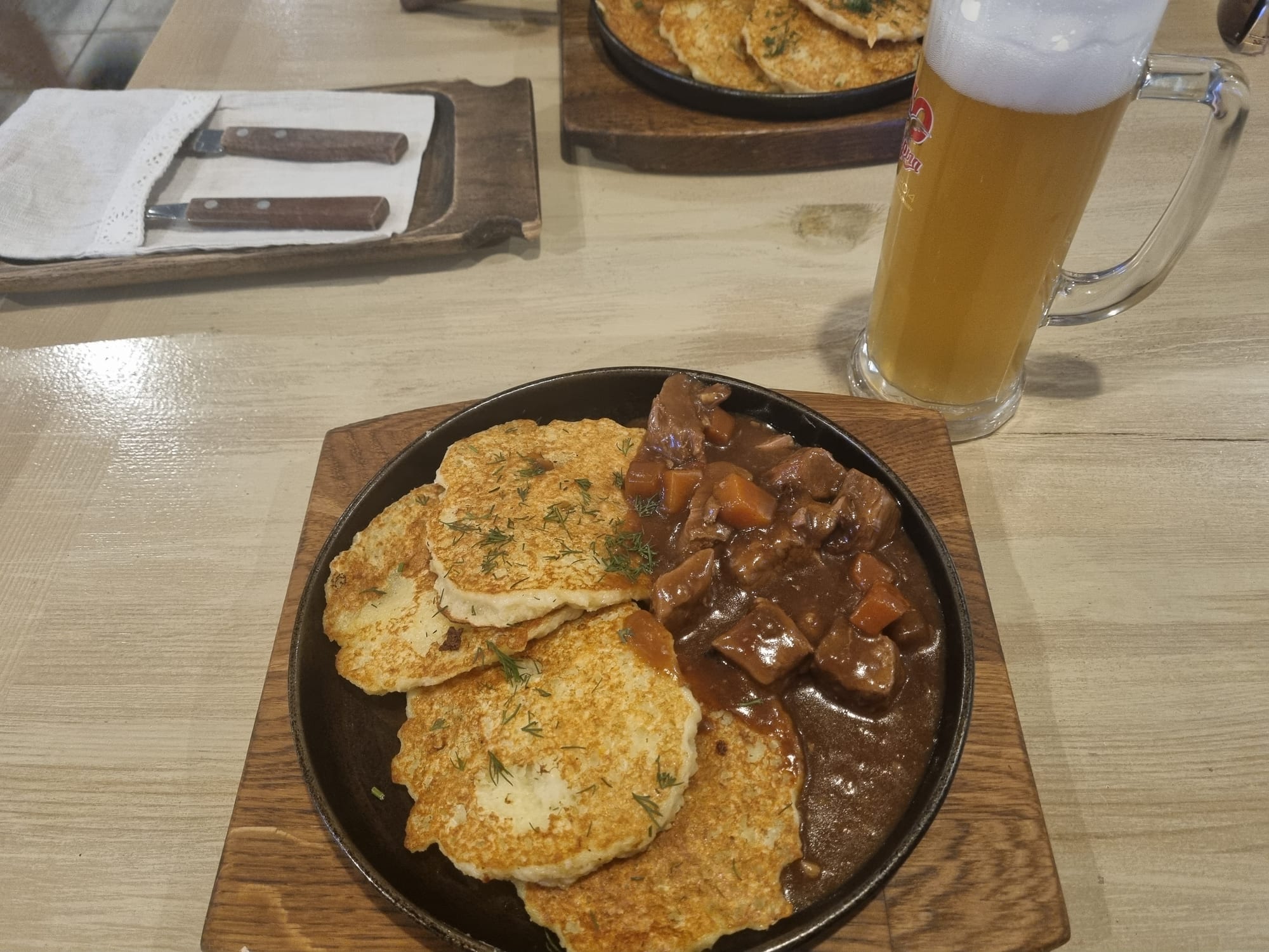 A plate of potato pancakes beside a bowl of beef goulash, in a restaurant setting