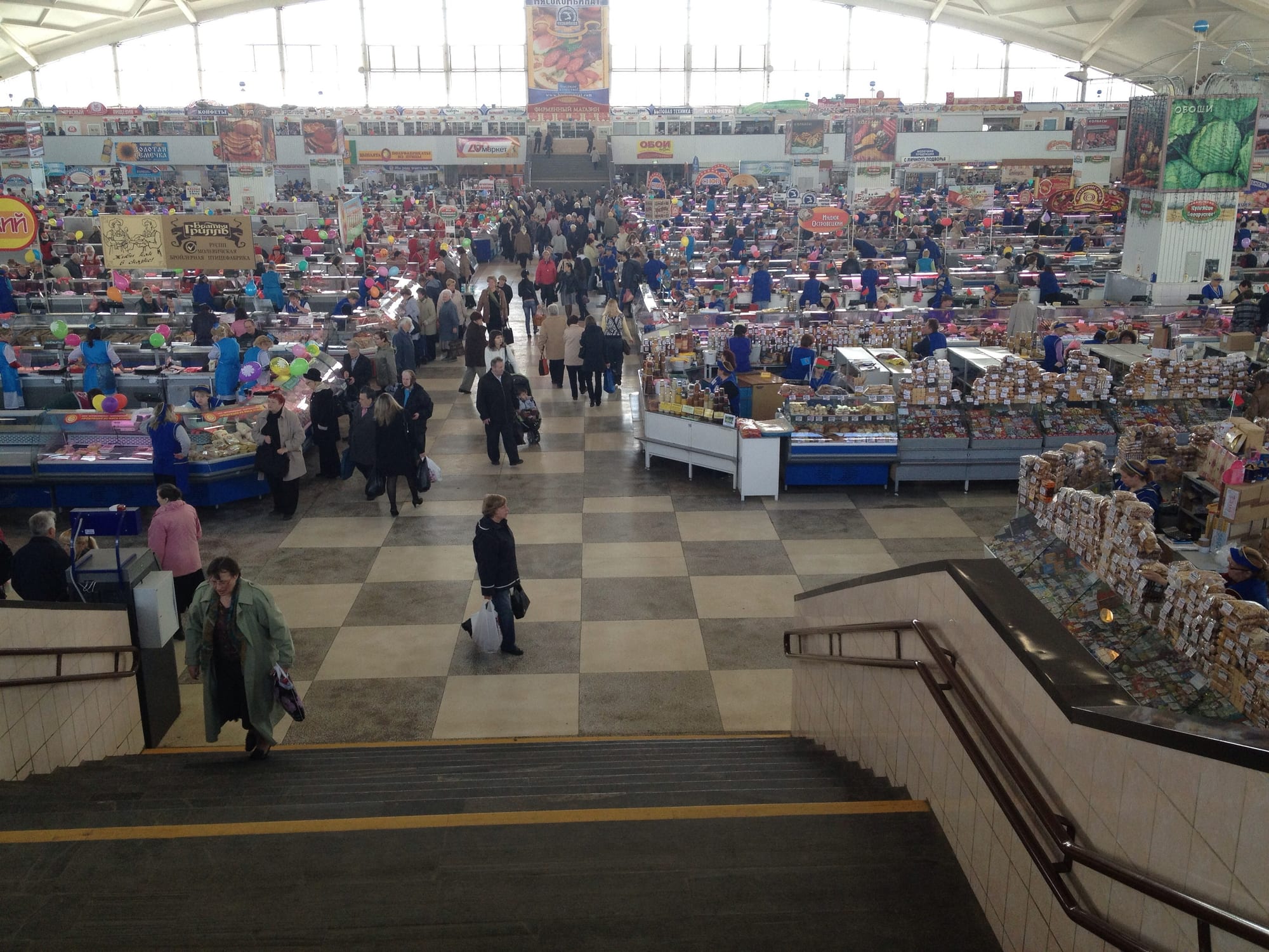 An elevated view of a large indoor market hall crowded with shoppers, meat and produce counters, and vendor stalls