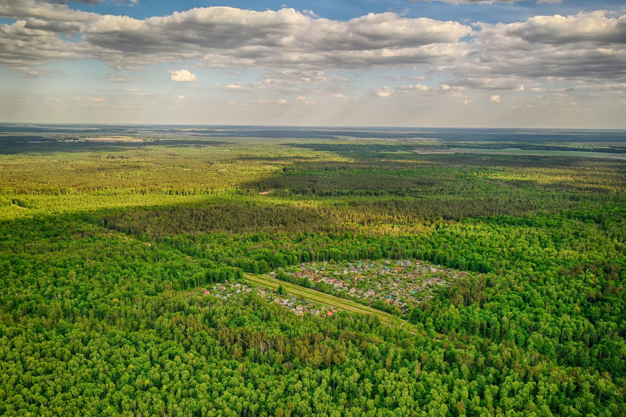An aerial view of a small settlement of dacha cottages with coloured roofs, surrounded on all sides by dense forest