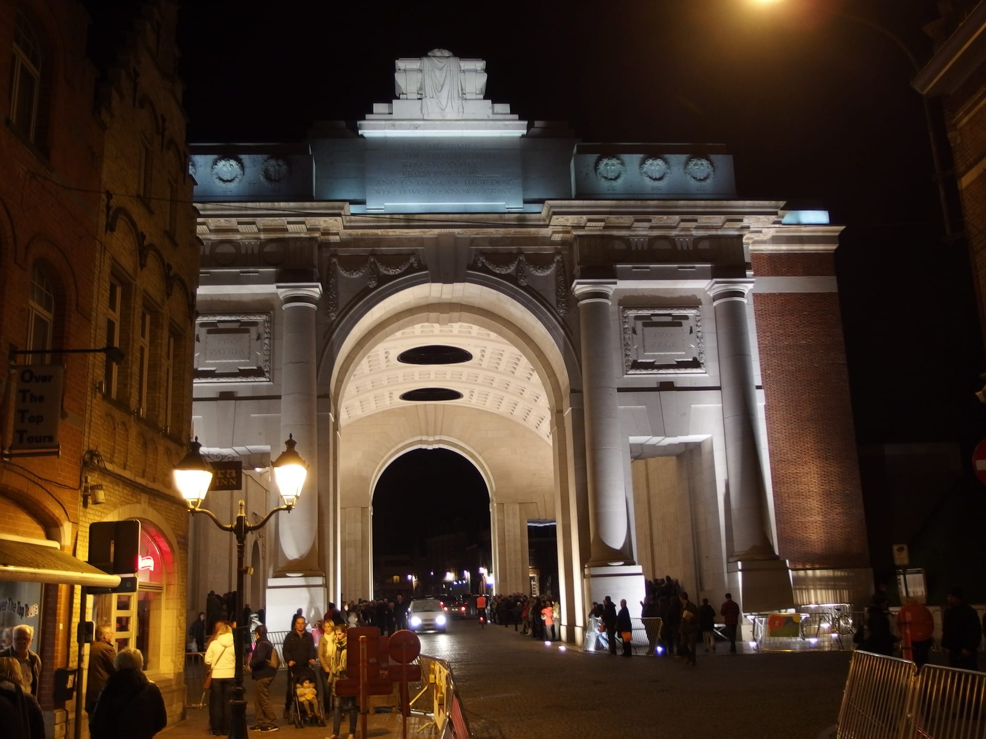 A large classical stone archway spanning a road, lit up at night with people passing beneath