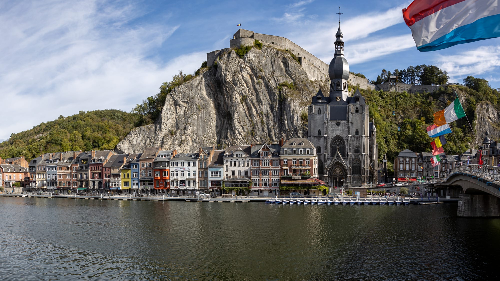 A bulb-domed church and a clifftop citadel above a row of tall houses on a green river