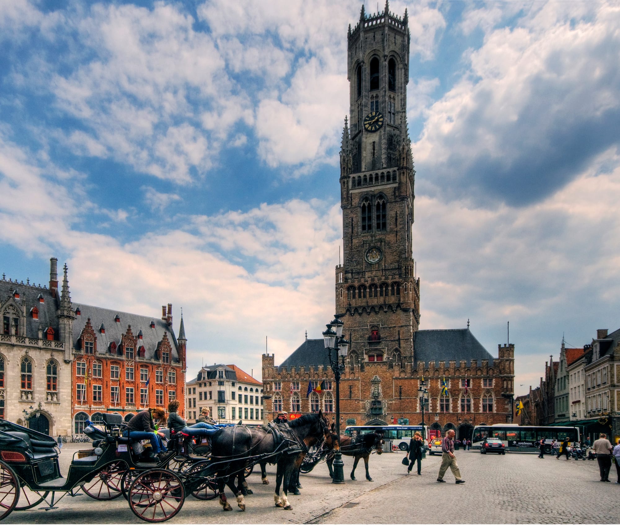 A medieval market square with a very tall leaning brick belfry and coloured gabled houses