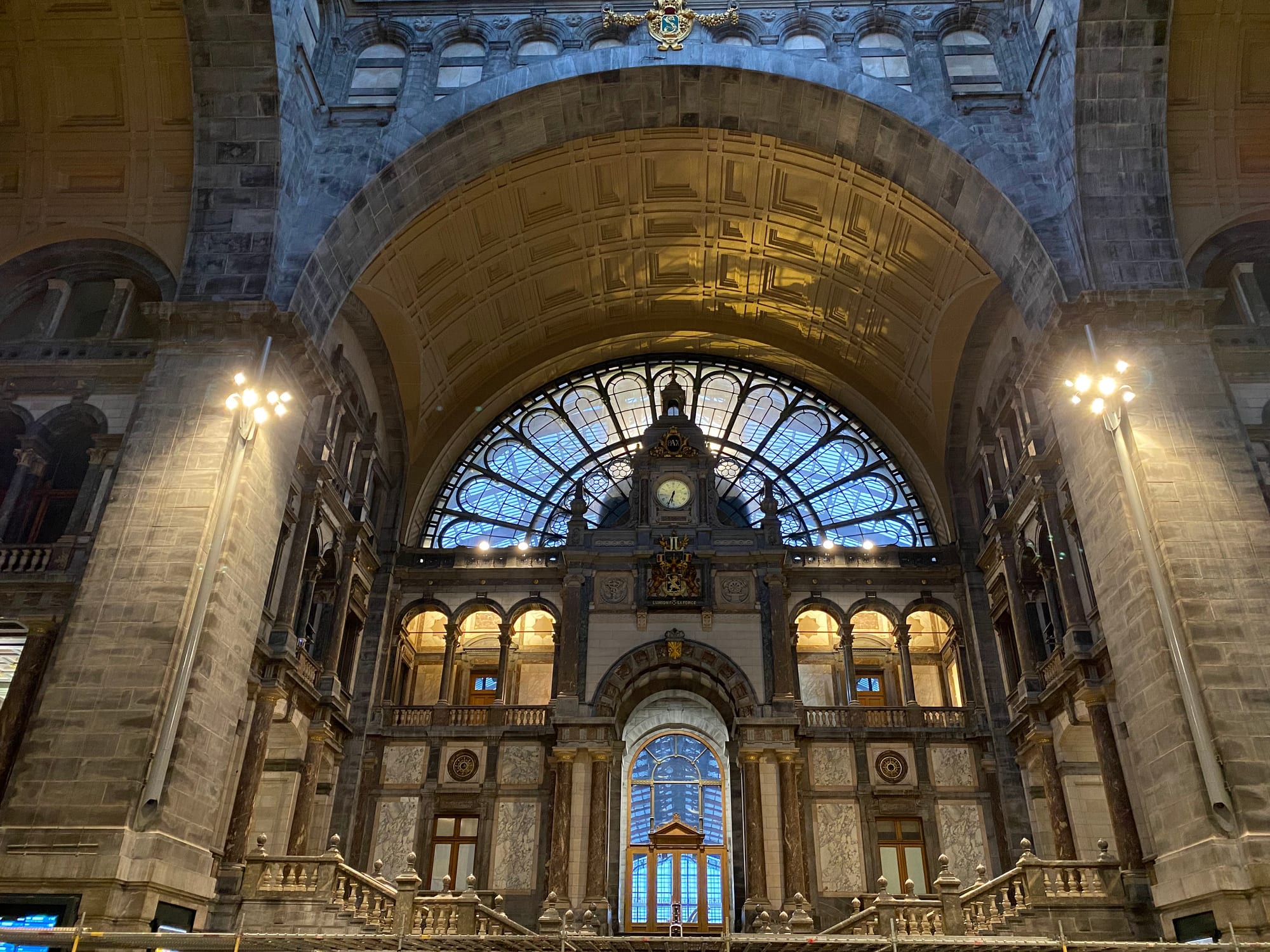 A vast stone railway hall with a domed glass roof, arched windows, and a grand staircase