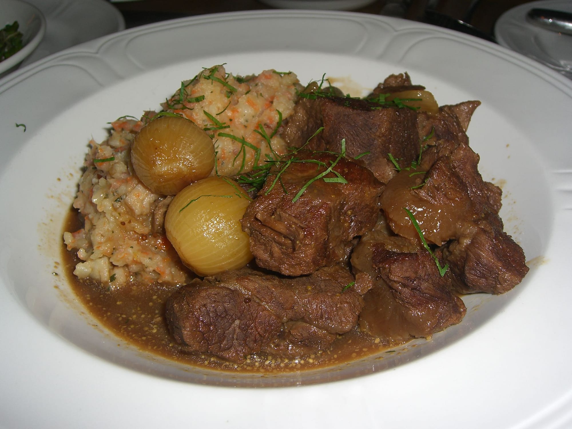 A dark, rich beef stew served beside a scoop of mashed potato mixed with vegetables
