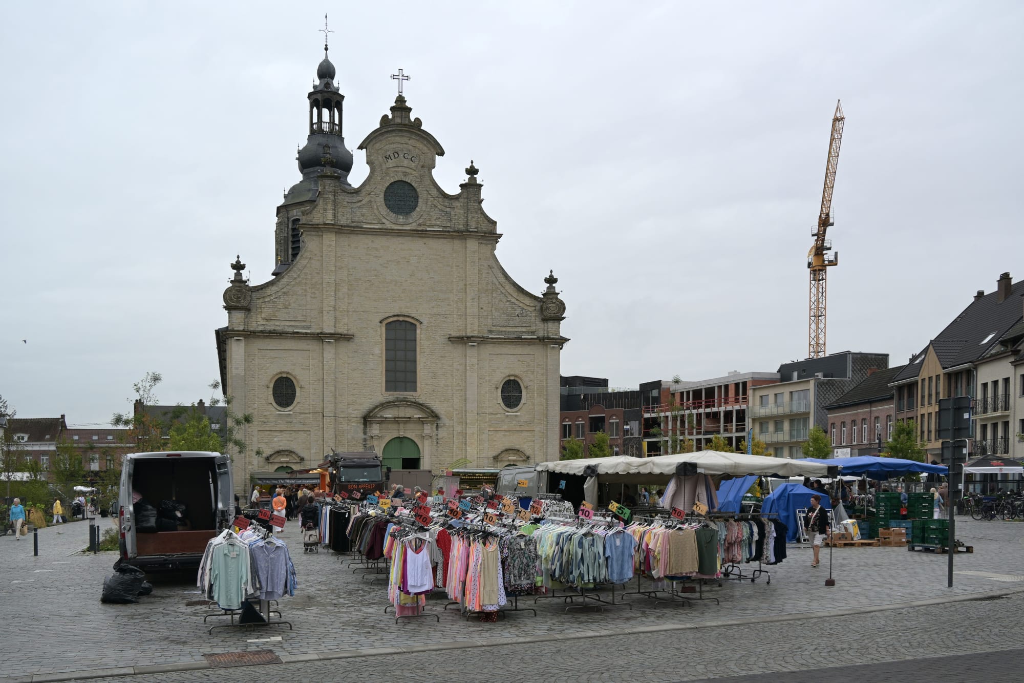Clothing racks and market stalls set up in a paved town square in front of a large baroque church