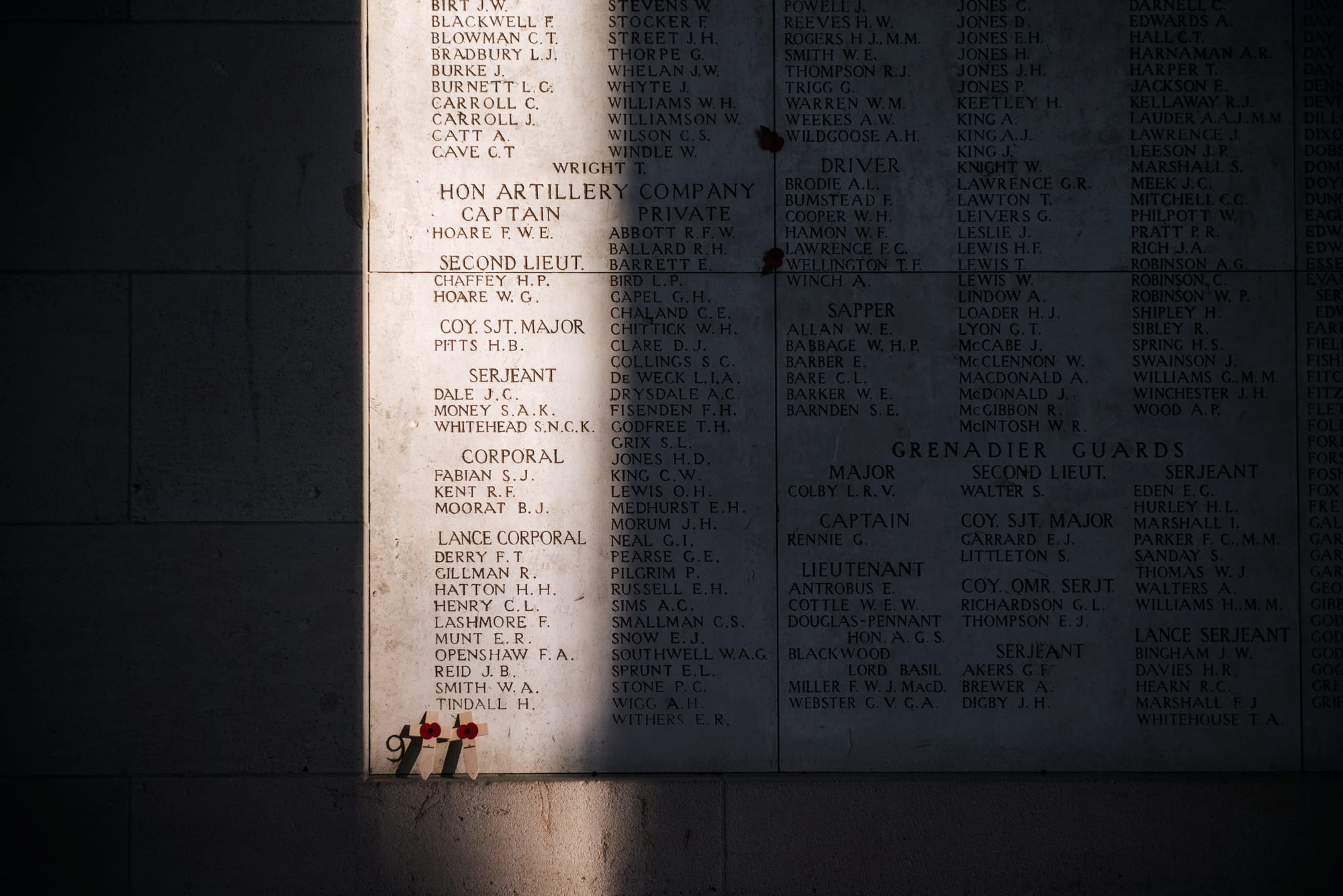 A large white stone triumphal arch memorial spanning a road, its walls covered in engraved names
