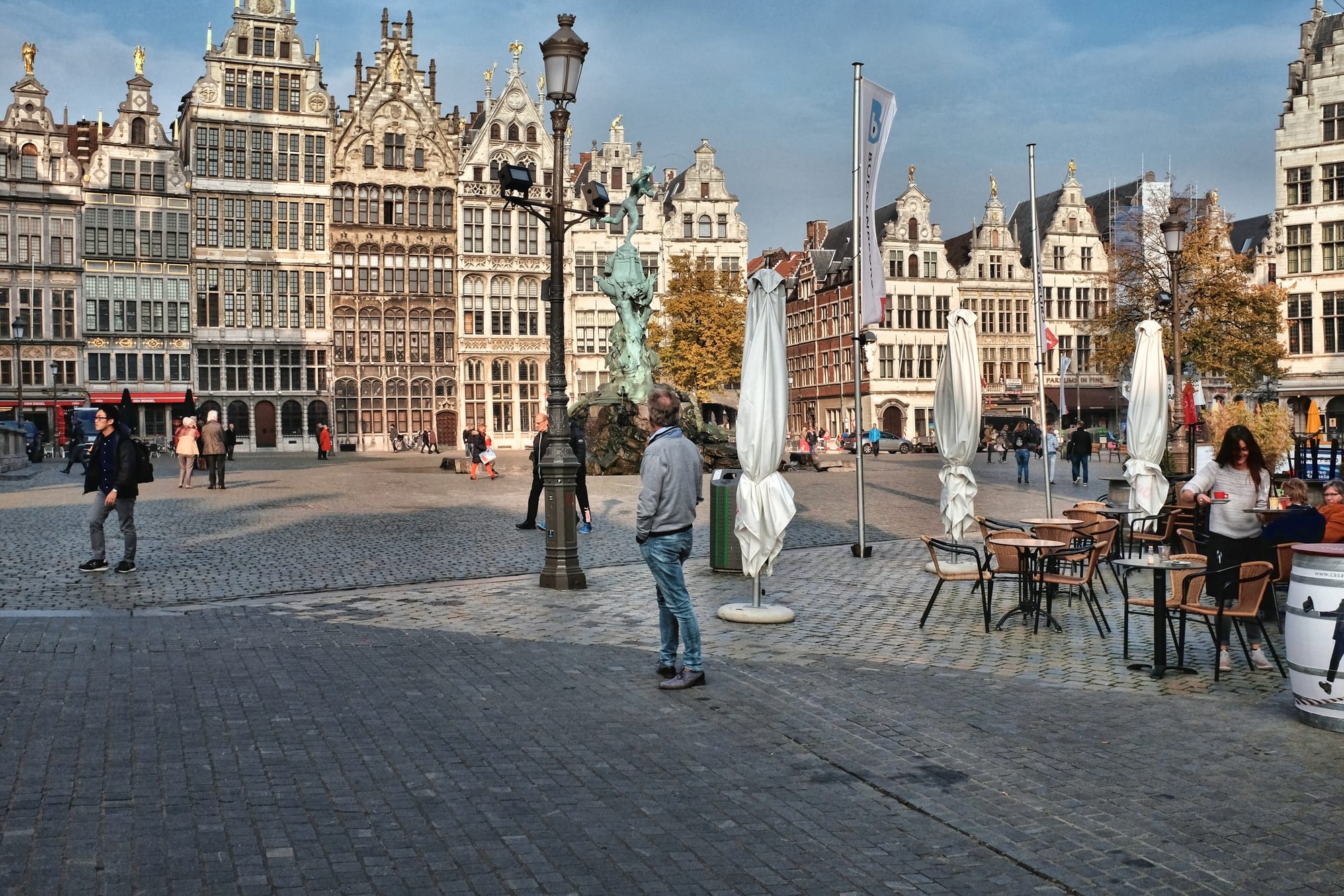 Tall narrow gabled guild houses with gilded statues around a market square, a cathedral spire behind