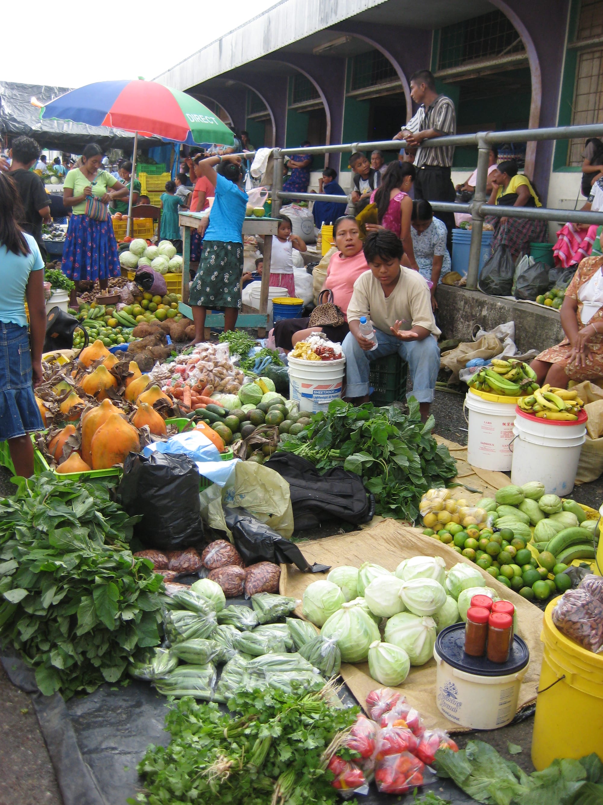 Vendors and shoppers at an open-air produce market in Punta Gorda, with papayas, cabbages, bananas and other fresh produce spread out for sale