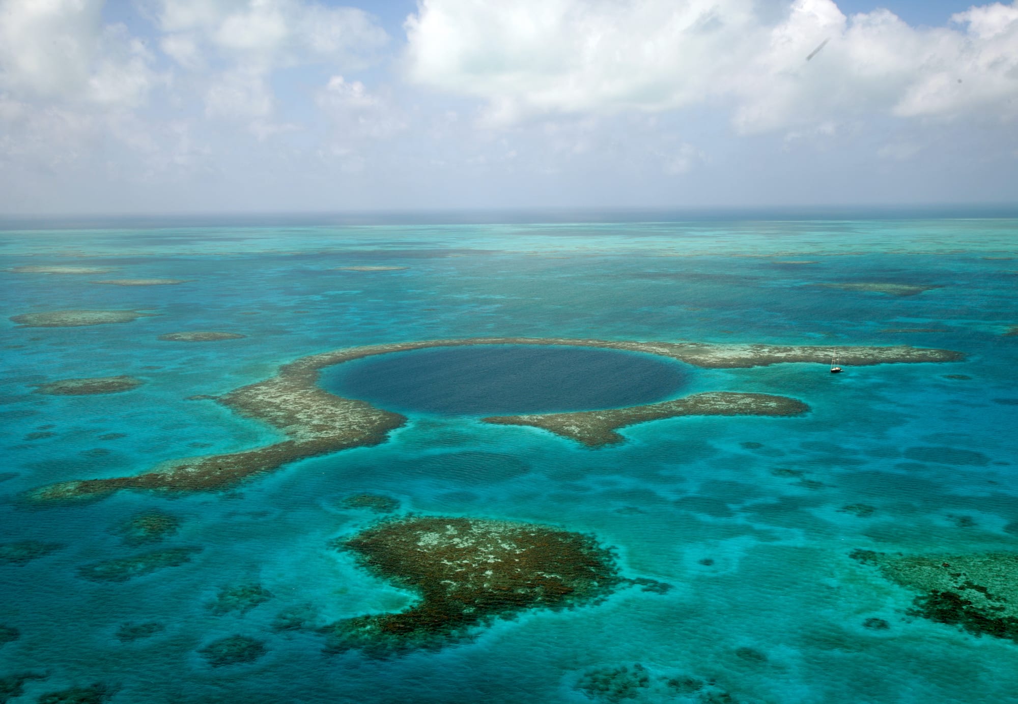 A near-perfect circle of deep navy water surrounded by pale turquoise reef, seen from the air