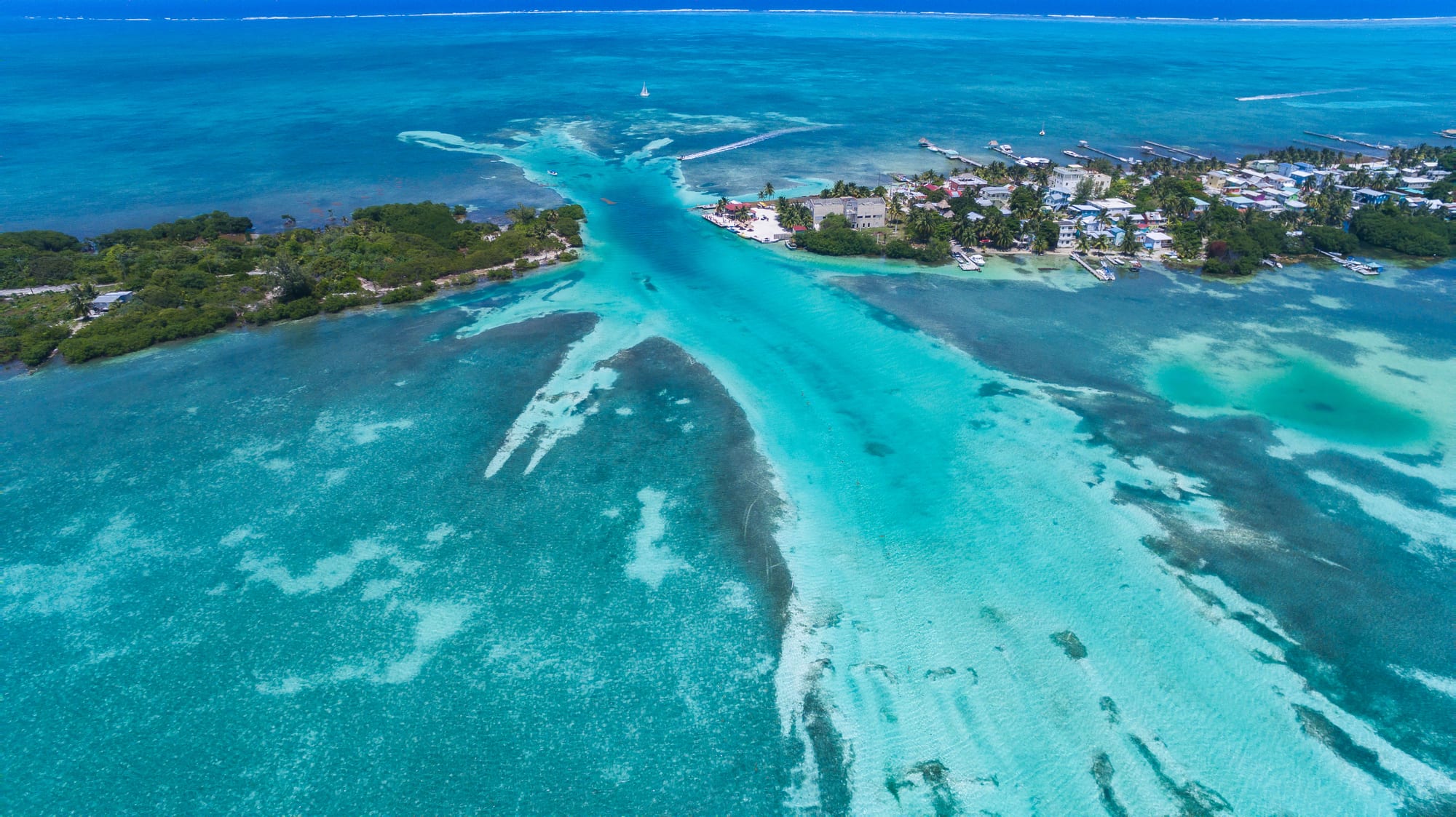 A thin sandy island covered in low buildings and palms, reef water on both sides