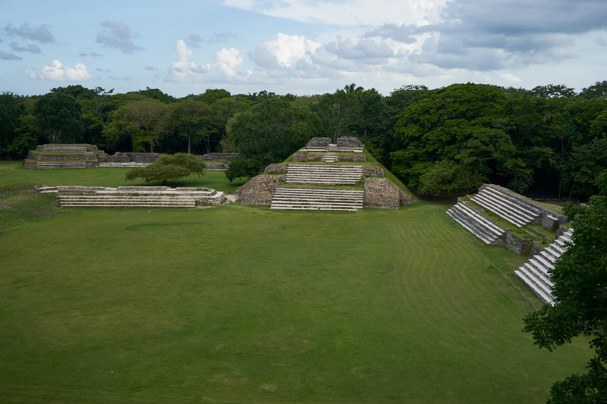 A broad low stone pyramid with a temple building on top, mown grass plaza around it