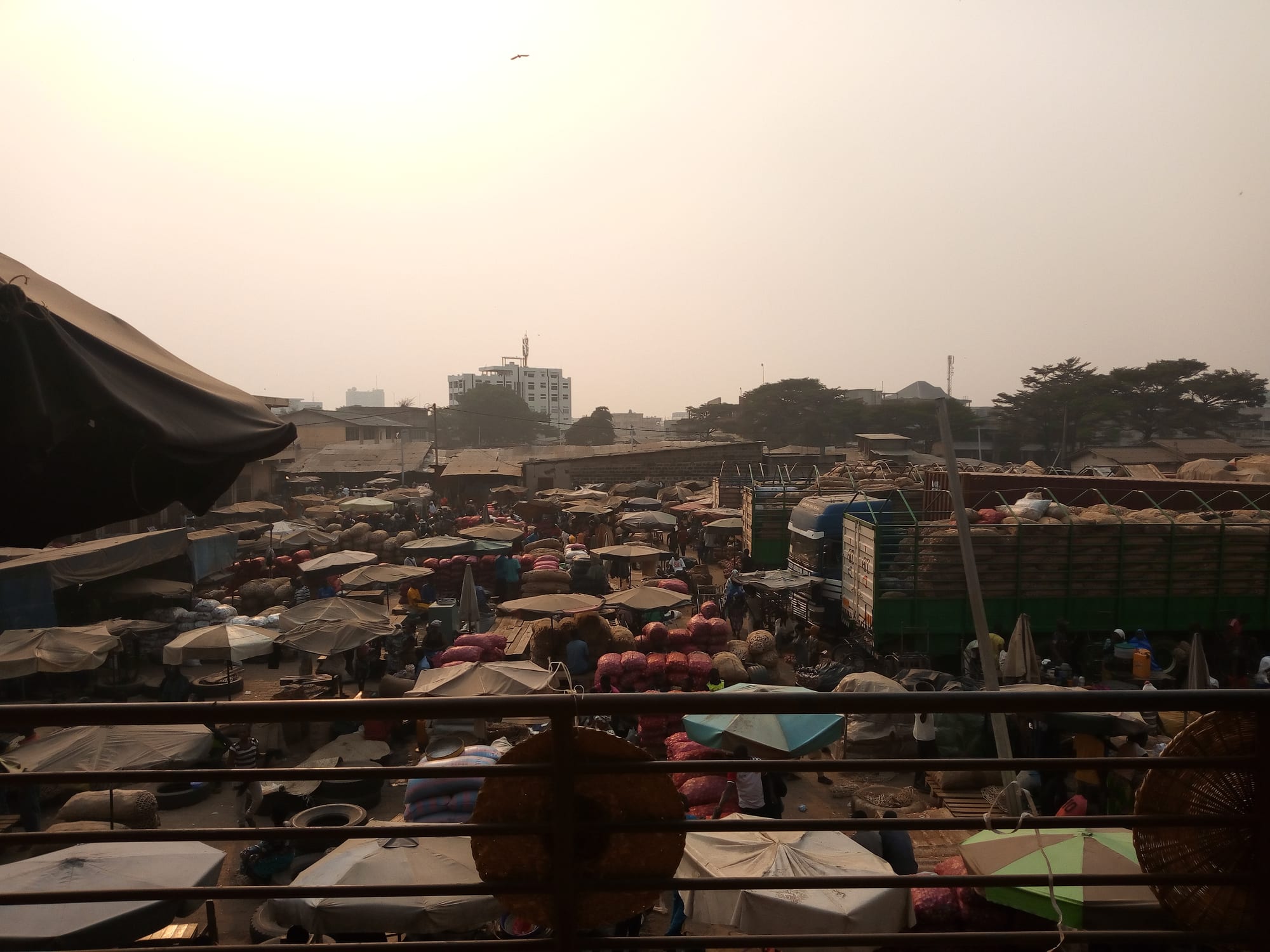 An elevated view over a sprawling open-air market packed with awnings, sacks of produce, trucks and crowds of people