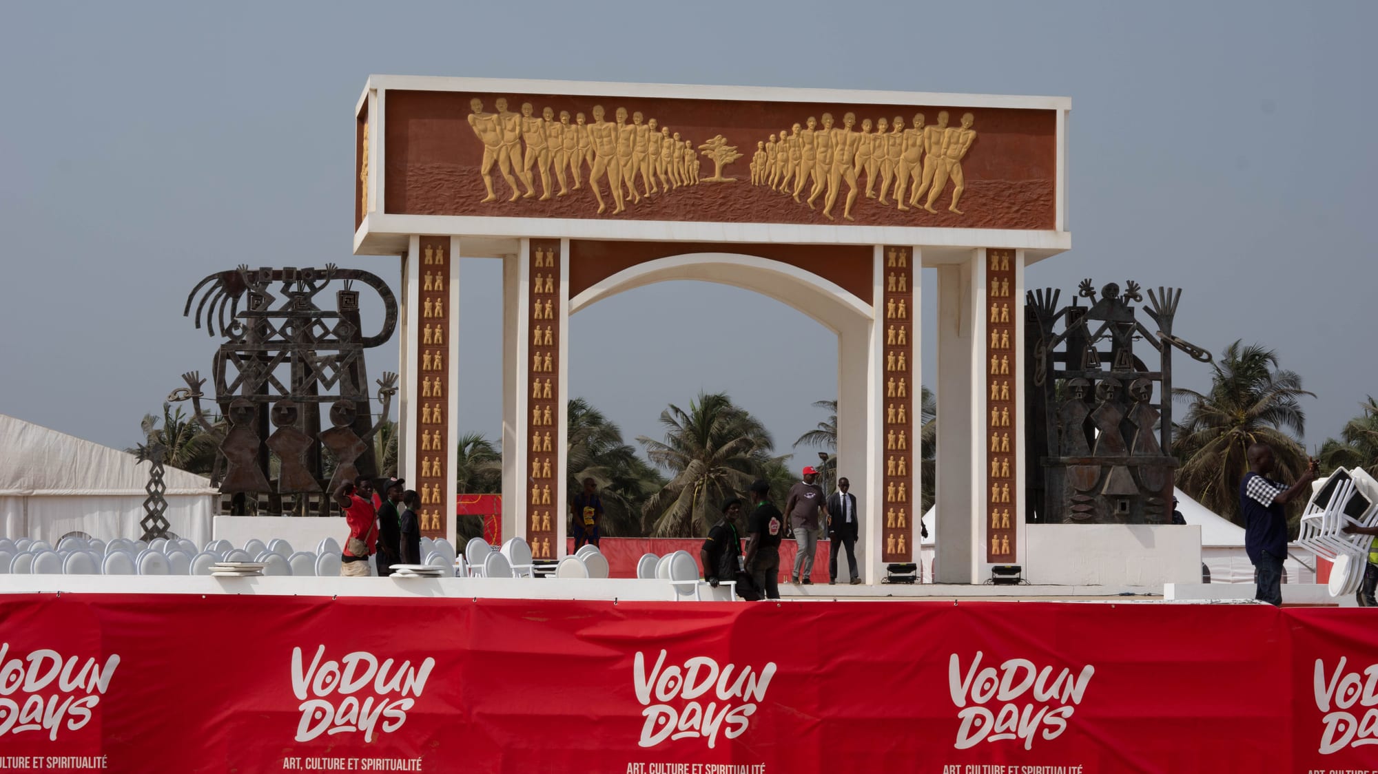 A large concrete arch monument with relief carvings, standing on a beach facing the sea