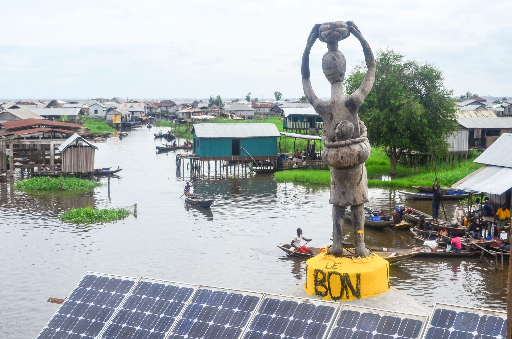 Wooden houses on stilts standing in open lake water, dugout canoes moving between them