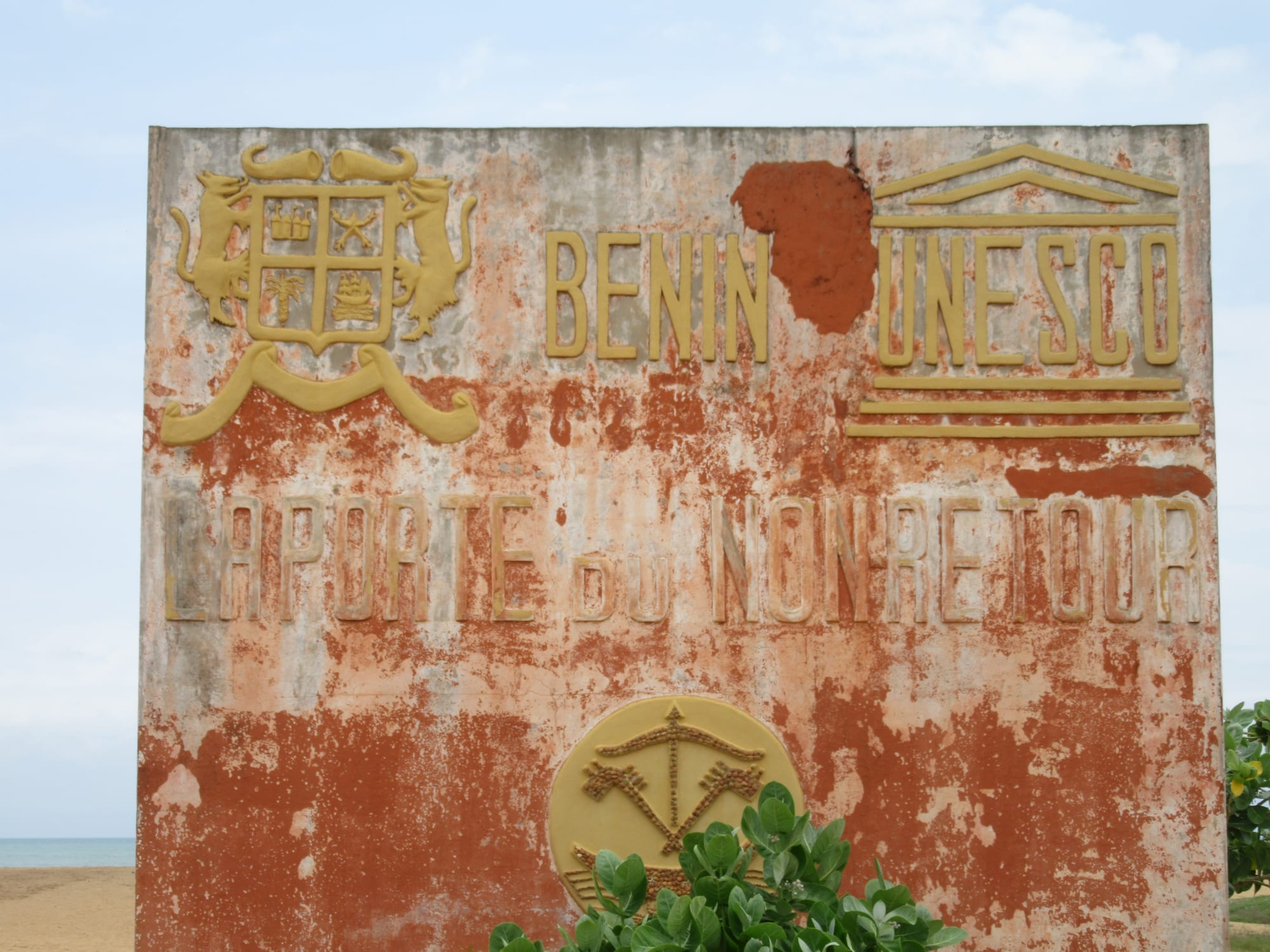 A large concrete archway monument with relief carvings standing on a wide empty beach facing the sea