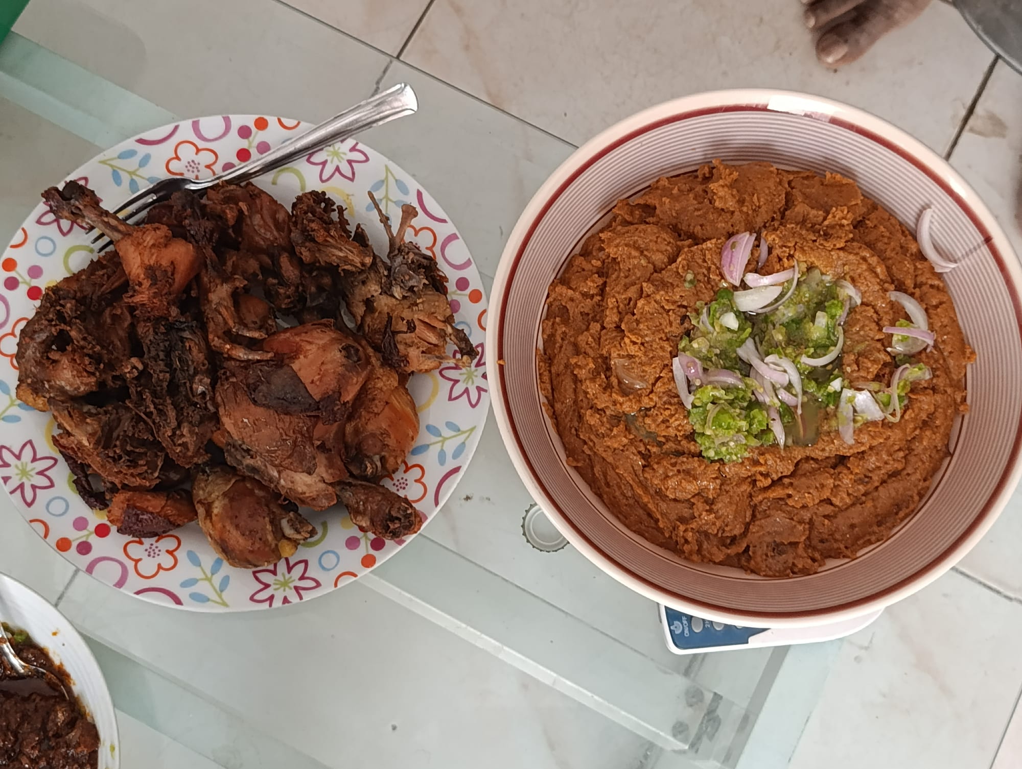 A plate of thick reddish-orange corn paste served with a piece of chicken in sauce