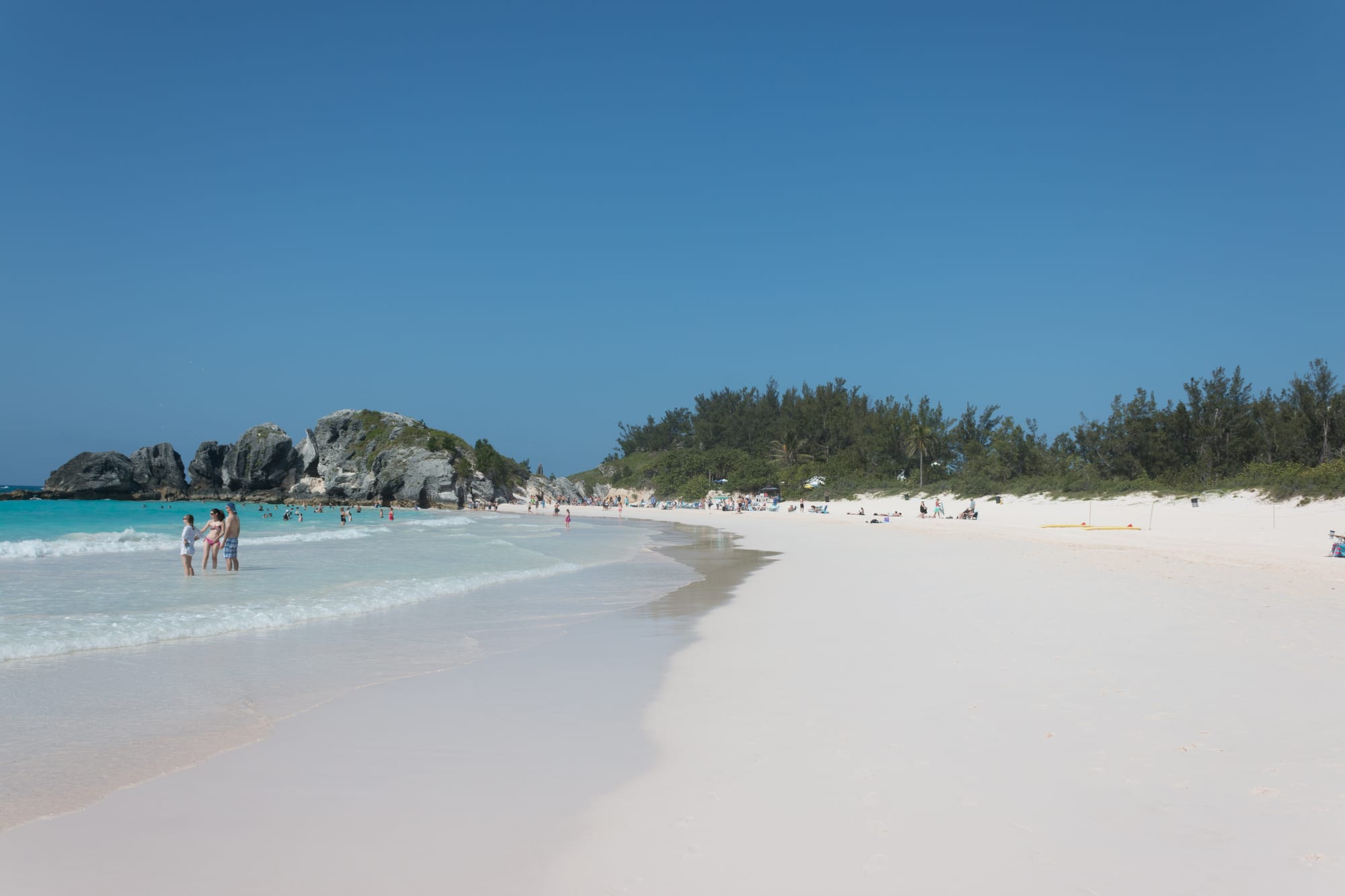 A broad crescent of pink-tinted sand backed by low limestone cliffs, turquoise water beyond
