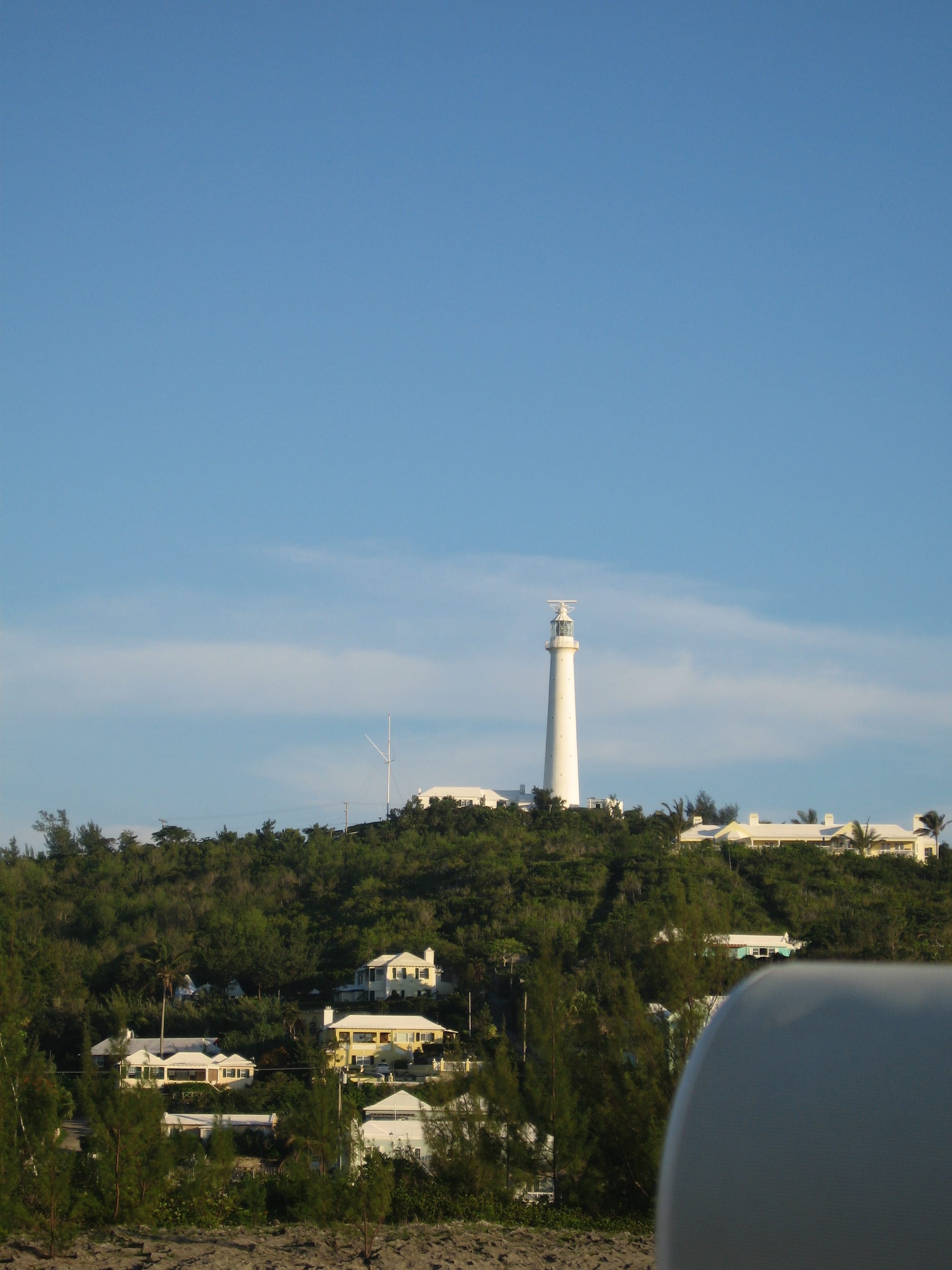 A tall white cast-iron lighthouse on a green hilltop against a blue sky