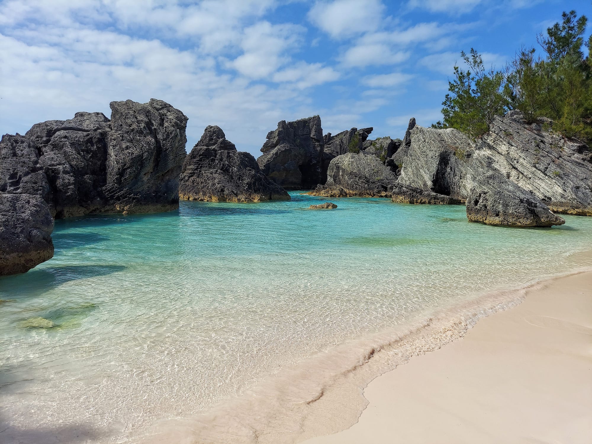 A curving cove of pale pink sand between rounded limestone rocks, turquoise water beyond