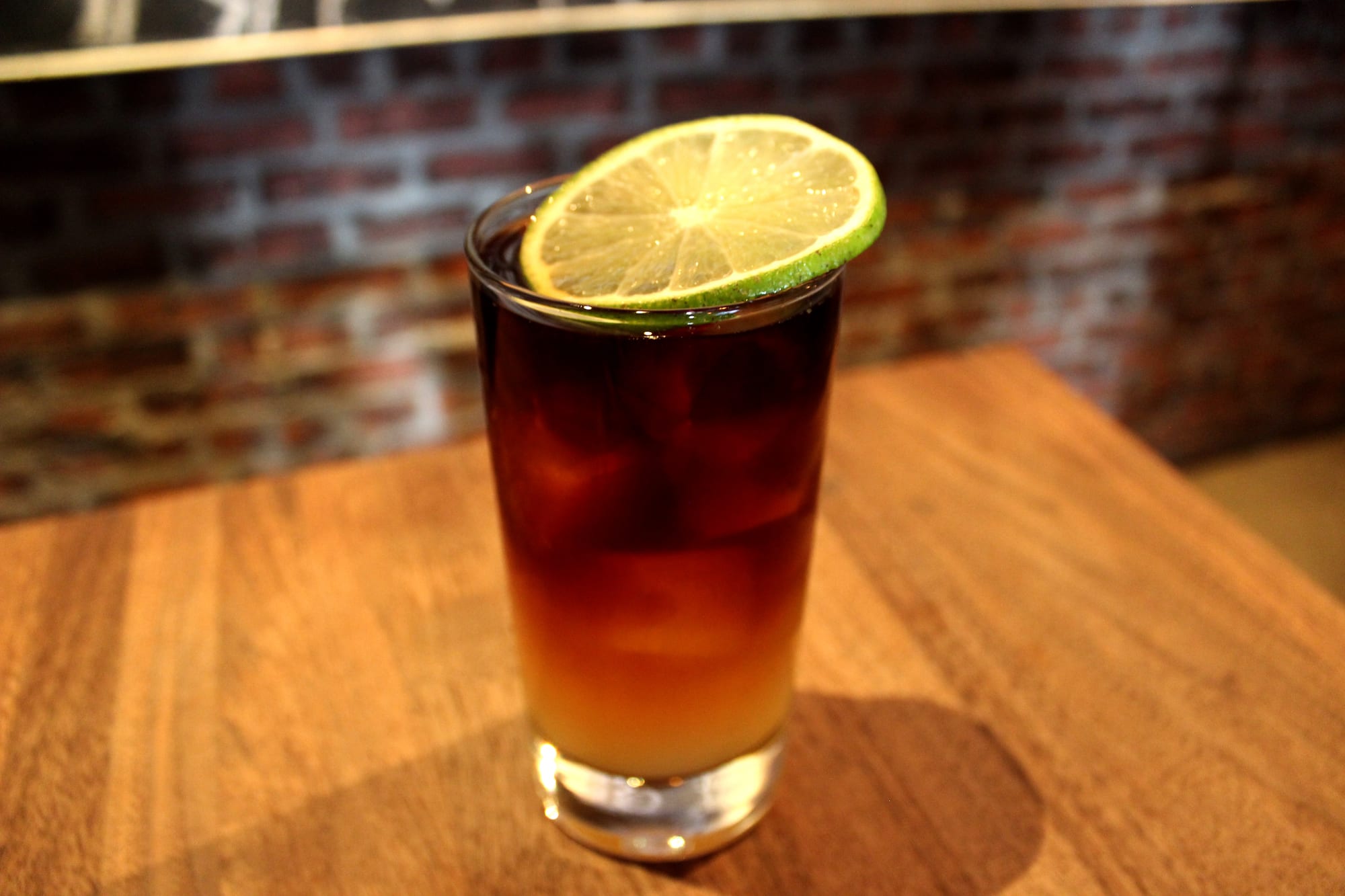 A tall glass of dark, cloudy amber drink with ice