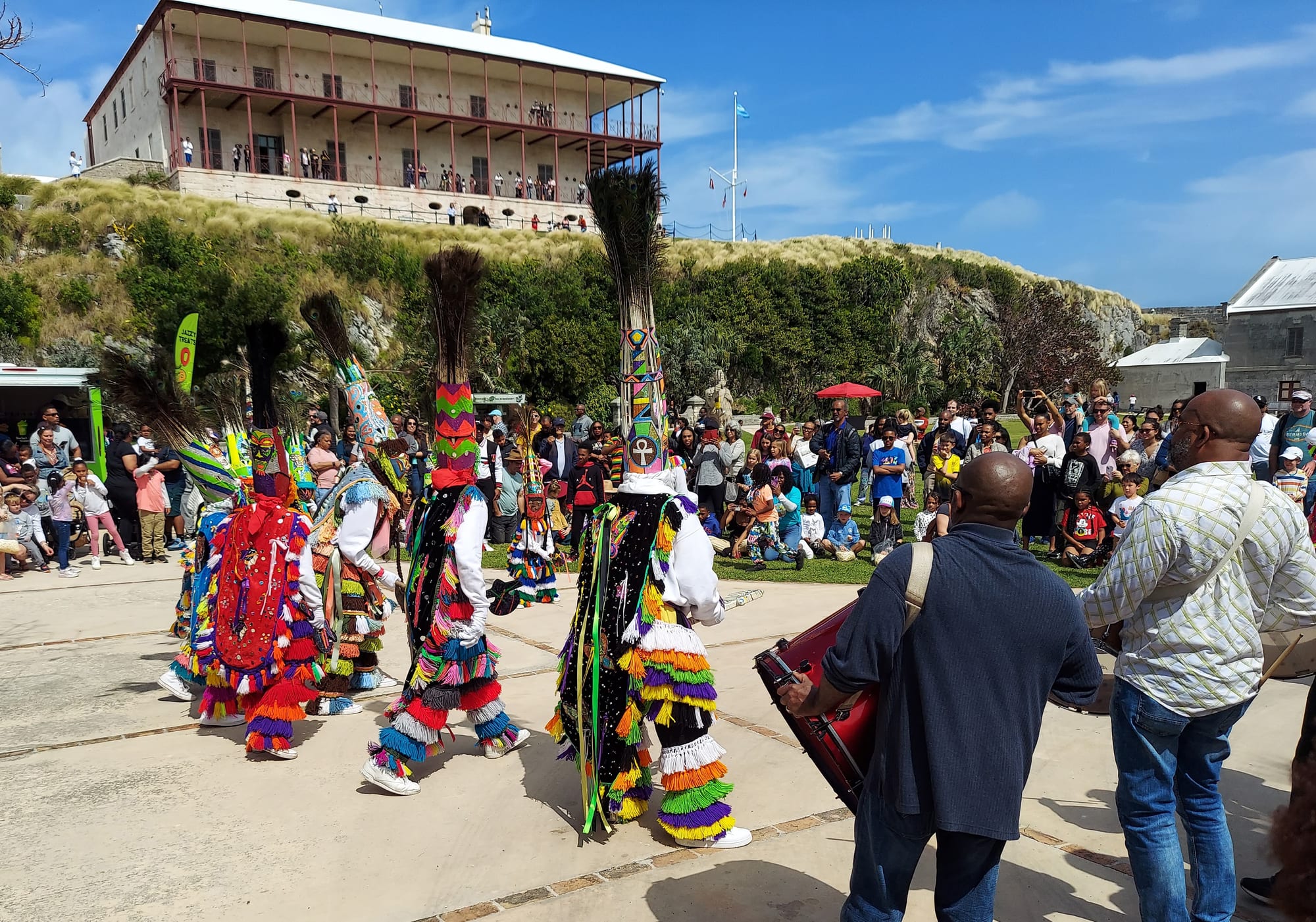 Dancers in tall feathered headdresses and bright fringed costumes performing with drums in a street