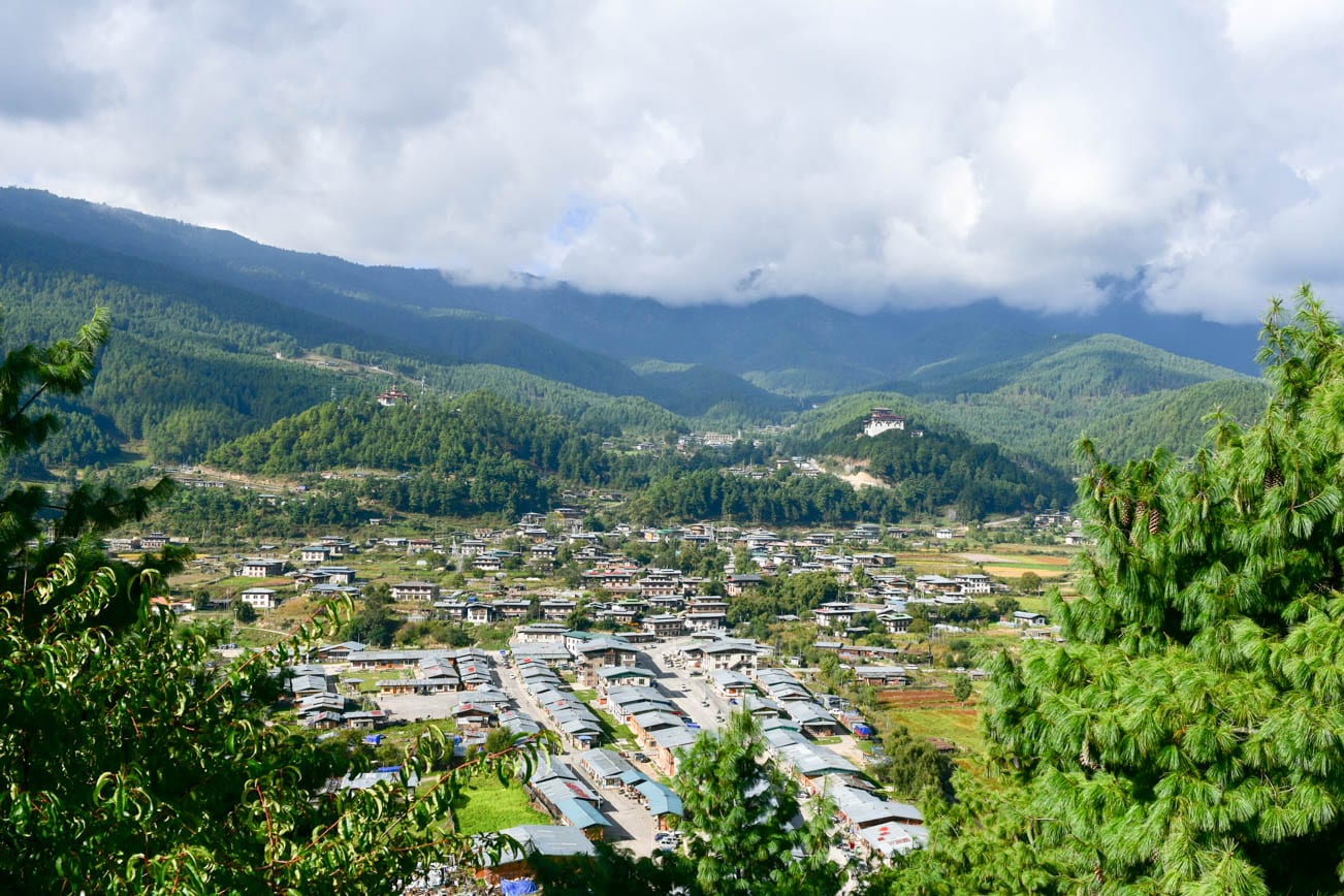 A small town of Bhutanese-style buildings spread across a wide valley of fields and pine
