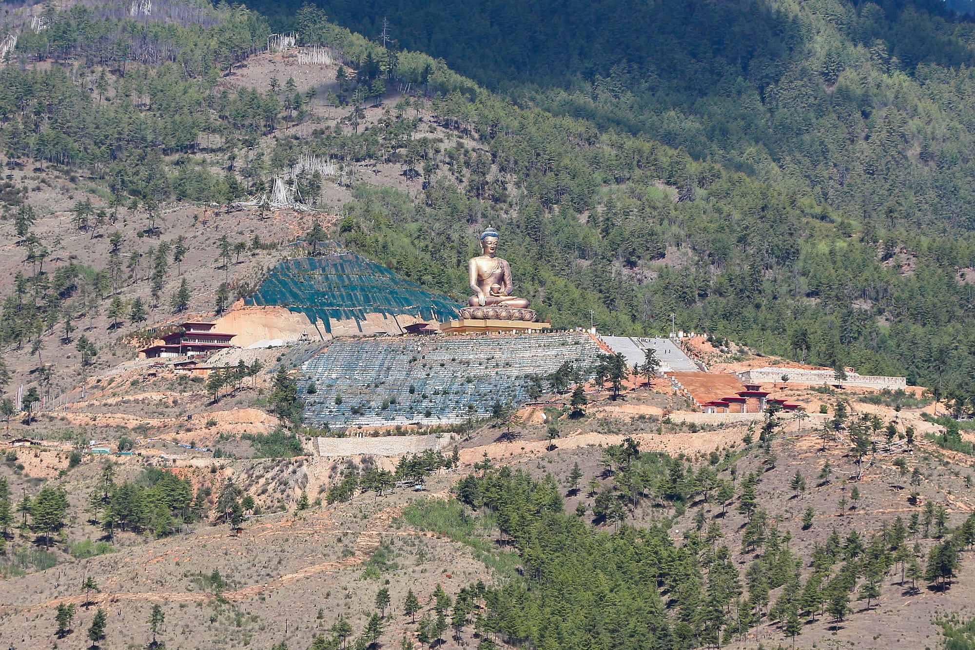 An enormous golden seated Buddha statue on a hilltop platform overlooking a valley