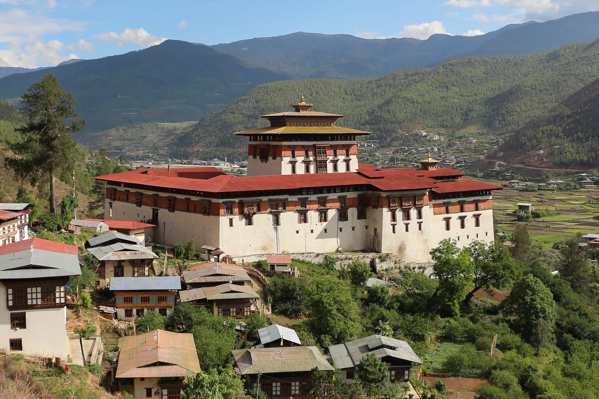 A large white fortress-monastery with sloping walls above a river and a covered wooden bridge