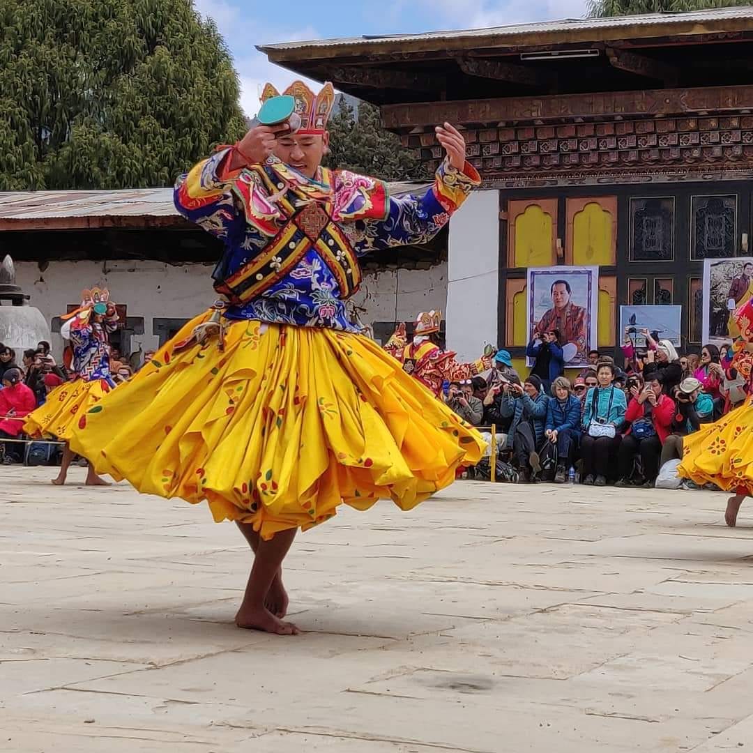 A masked dancer in bright layered silk robes mid-spin in a monastery courtyard