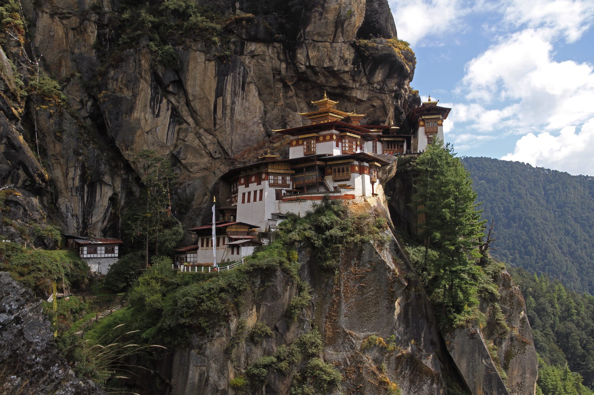 A whitewashed monastery of several buildings clinging to a sheer granite cliff high above a forested valley