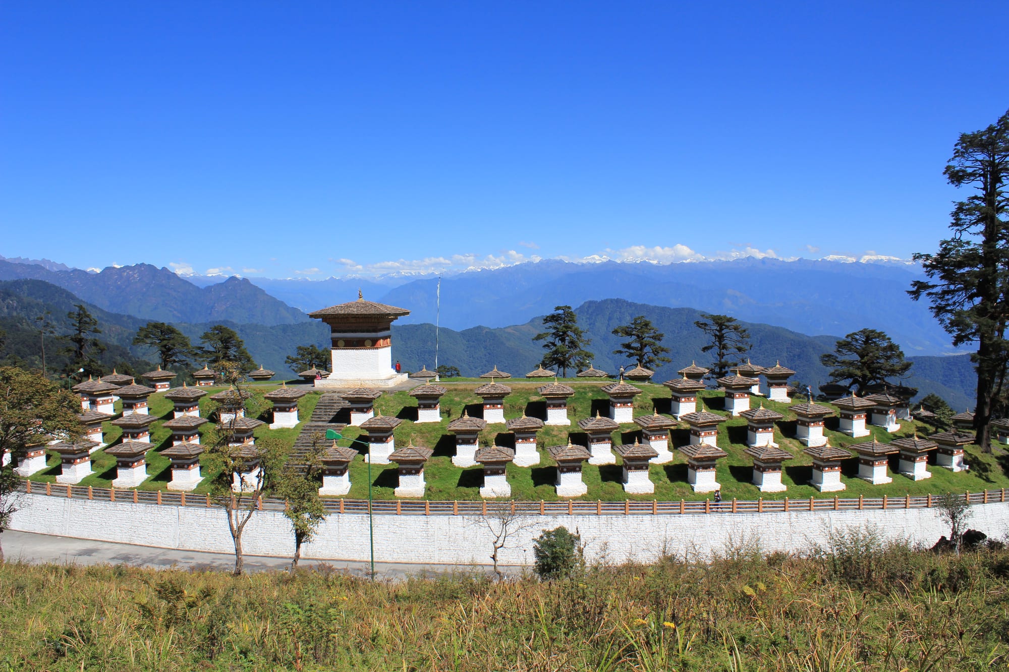 More than a hundred small stone stupas clustered on a hilltop, forested ridges and snow peaks beyond