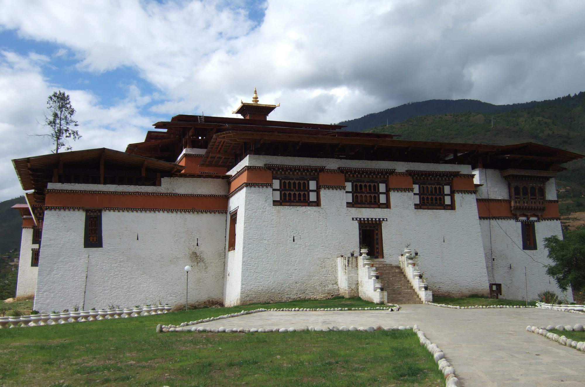 A compact whitewashed fortress with a red band under dark timber roofs, set on a grassy rise with a stone stairway to its door