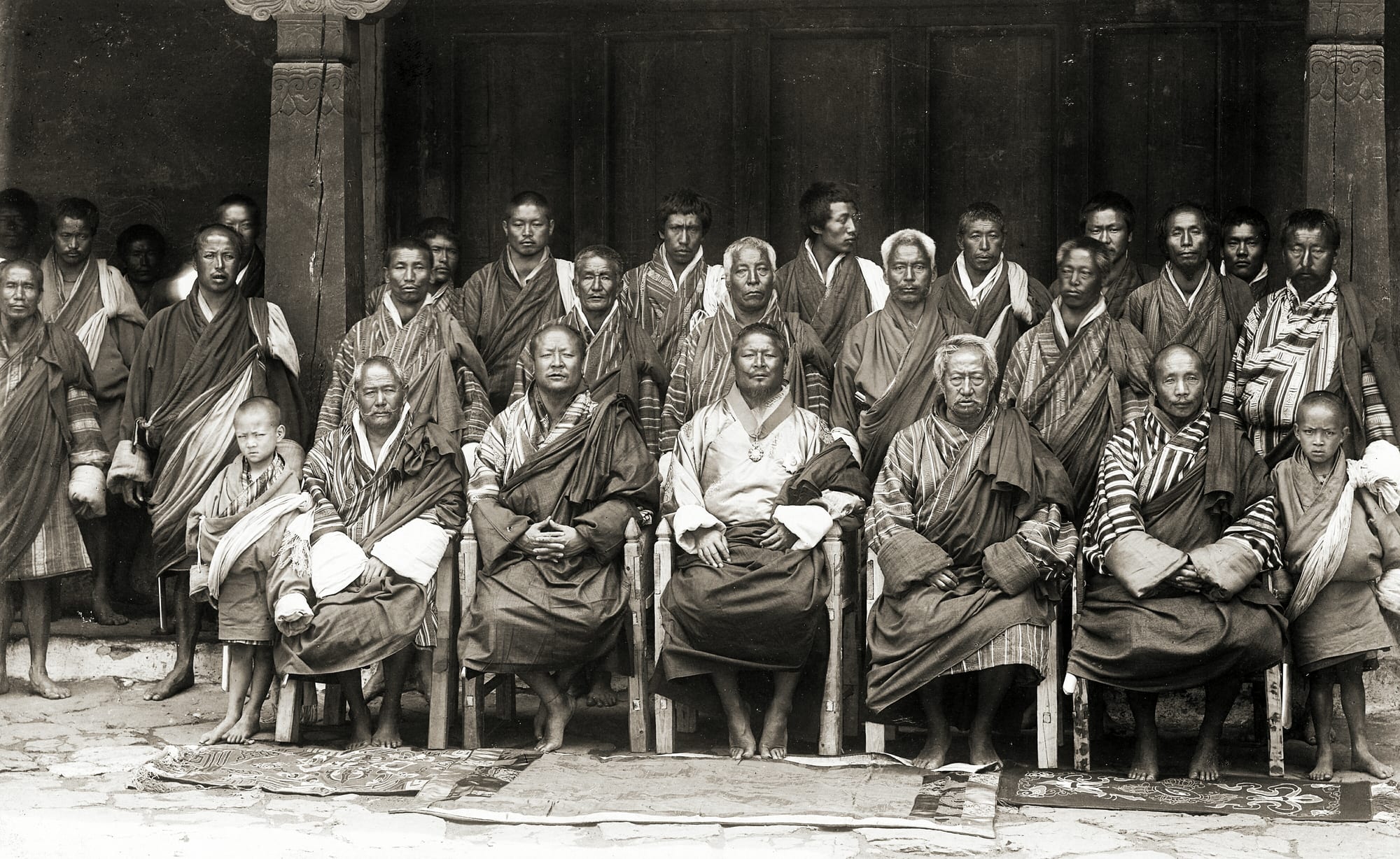 A 1905 photograph of a seated Bhutanese ruler in silk robes surrounded by officials in traditional dress