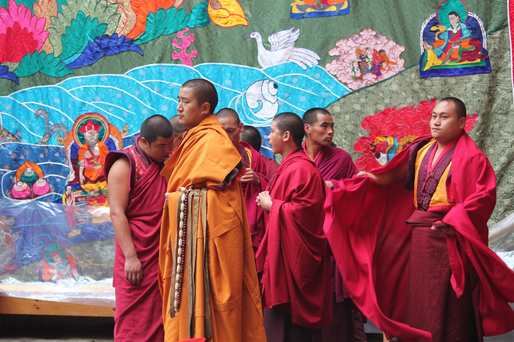 Monks in bright brocade robes and masks performing a dance in a monastery courtyard before a crowd