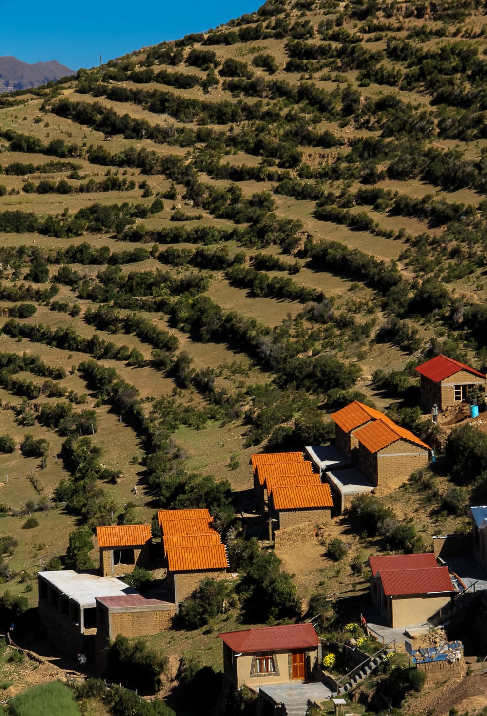 Ancient farming terraces and stone houses on a hillside above deep-blue lake water